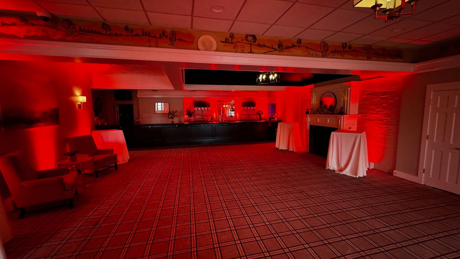An empty room with red lights on the ceiling and tables and chairs.