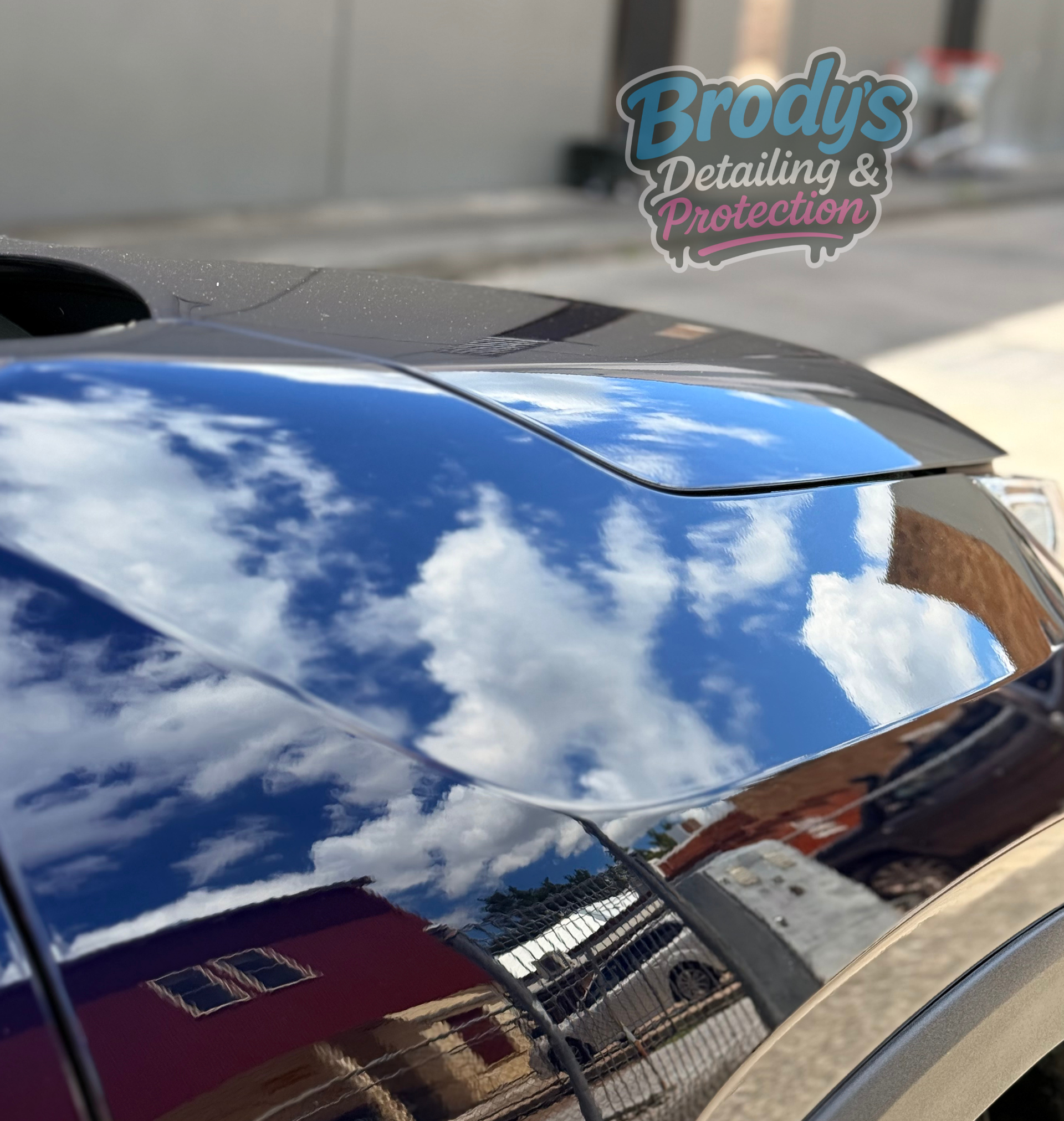 Black car hood reflects blue sky and clouds;
