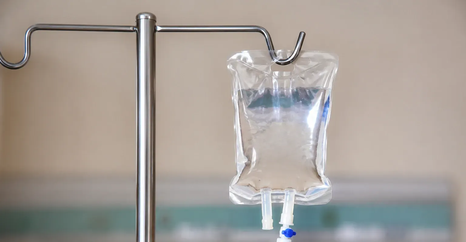 IV drip bag hanging from a metal pole with blue liquid in the tubing