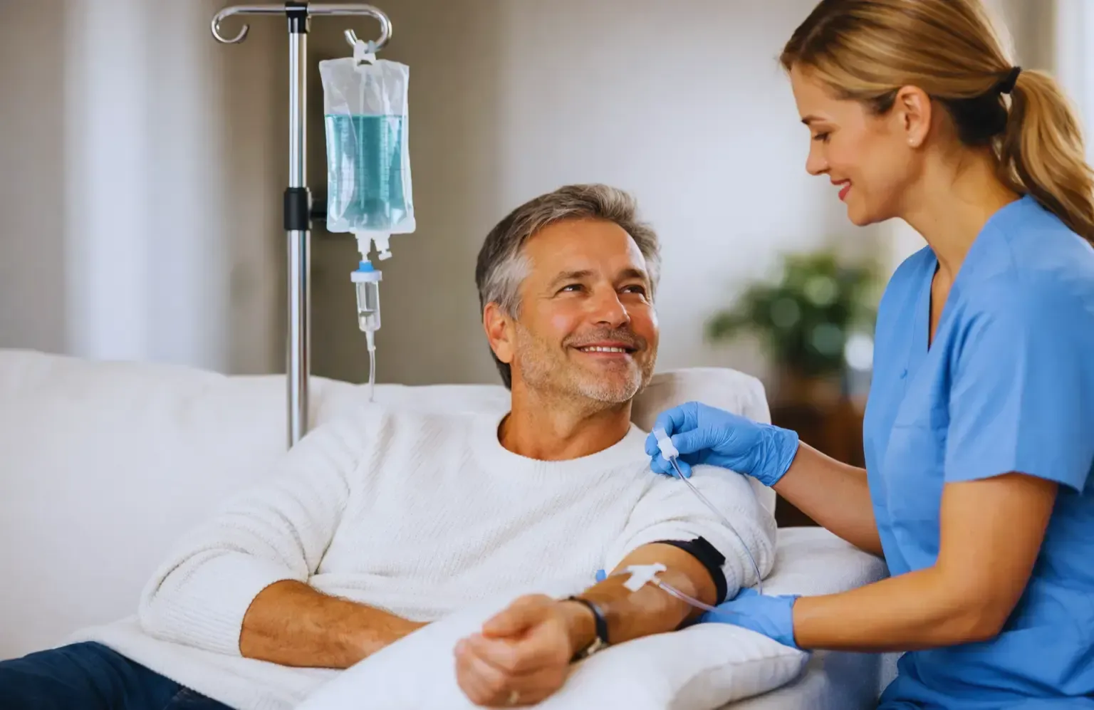 Nurse in blue scrubs comforting a smiling patient in a hospital bed beside an IV drip