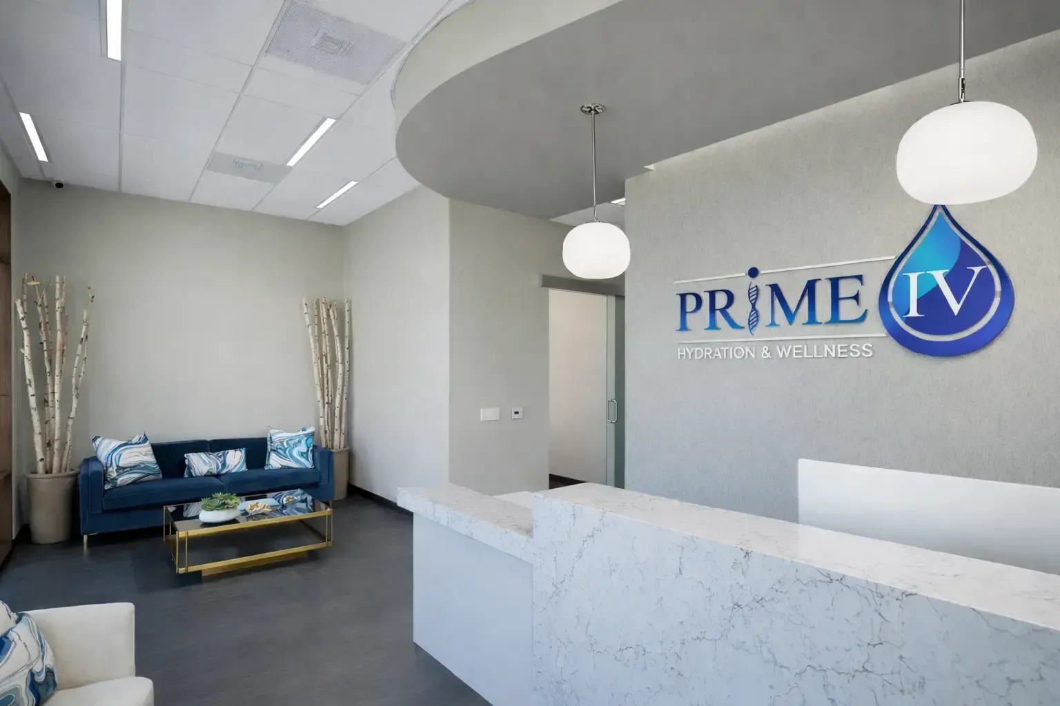 Modern clinic reception with white marble desk, blue seating, and “Prime IV” logo on the wall
