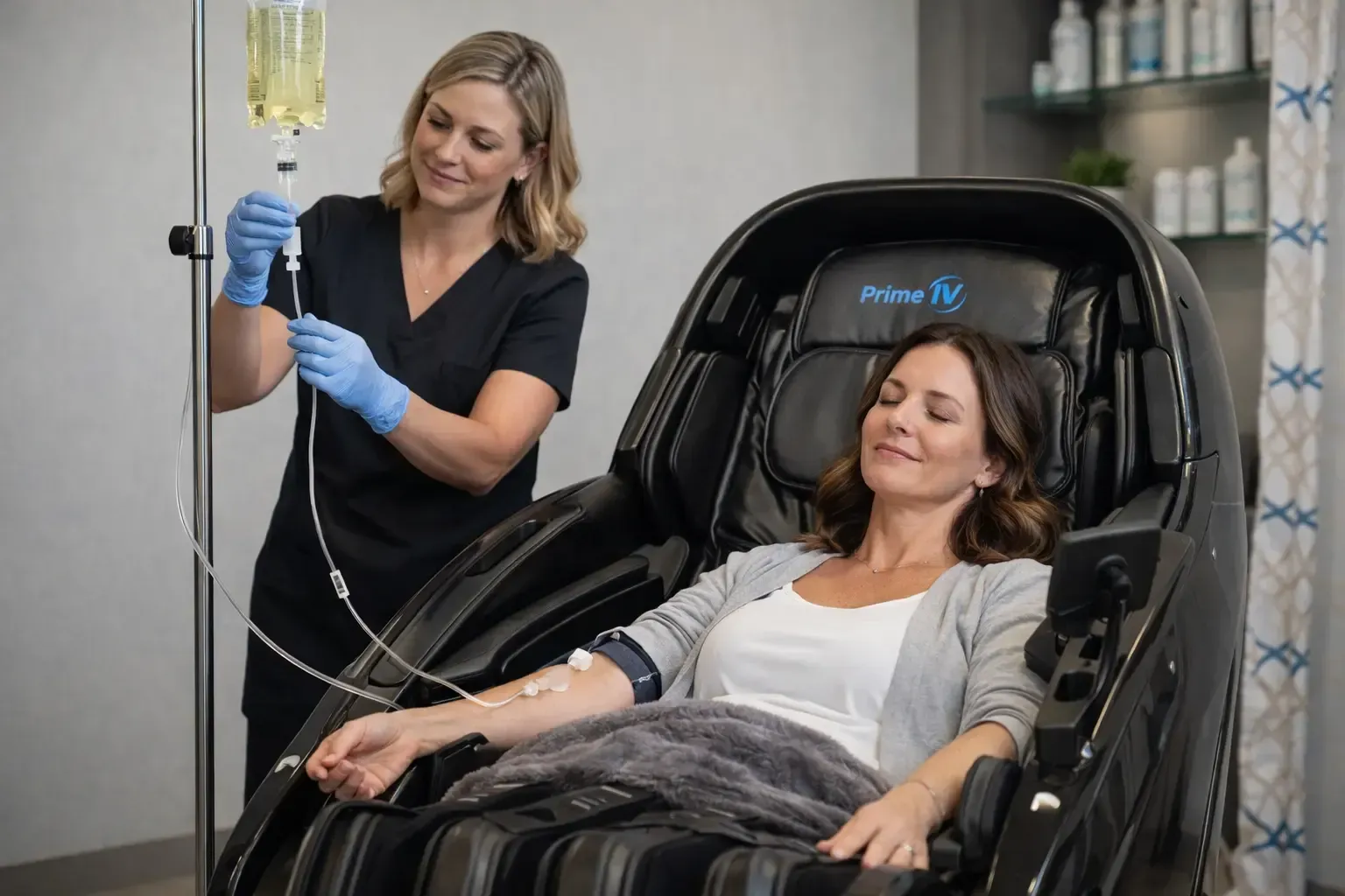 Woman reclining in a black treatment chair while a nurse adjusts an IV in a clinic setting