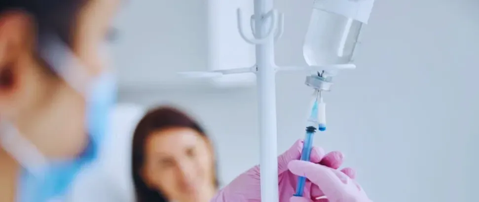 Close-up of gloved hands inserting a syringe into an IV drip in a hospital setting