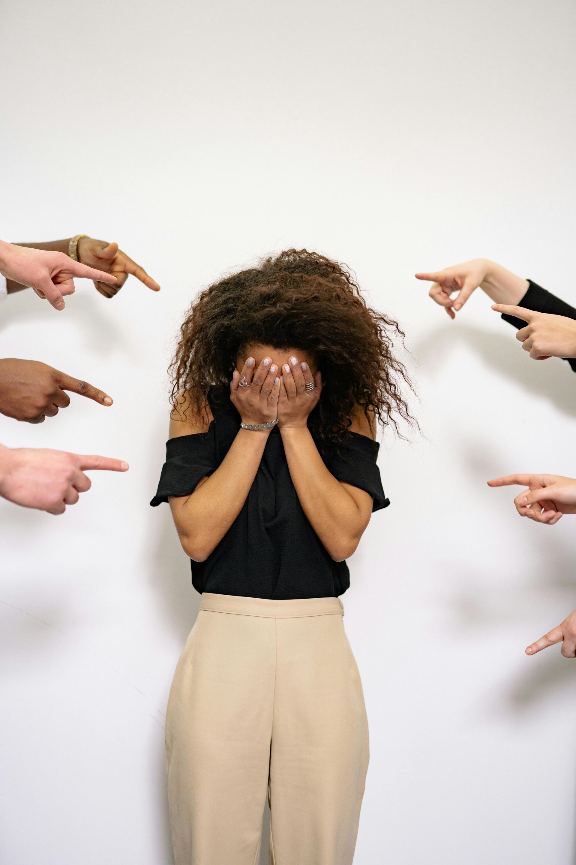 A woman is covering her face while people point at her.