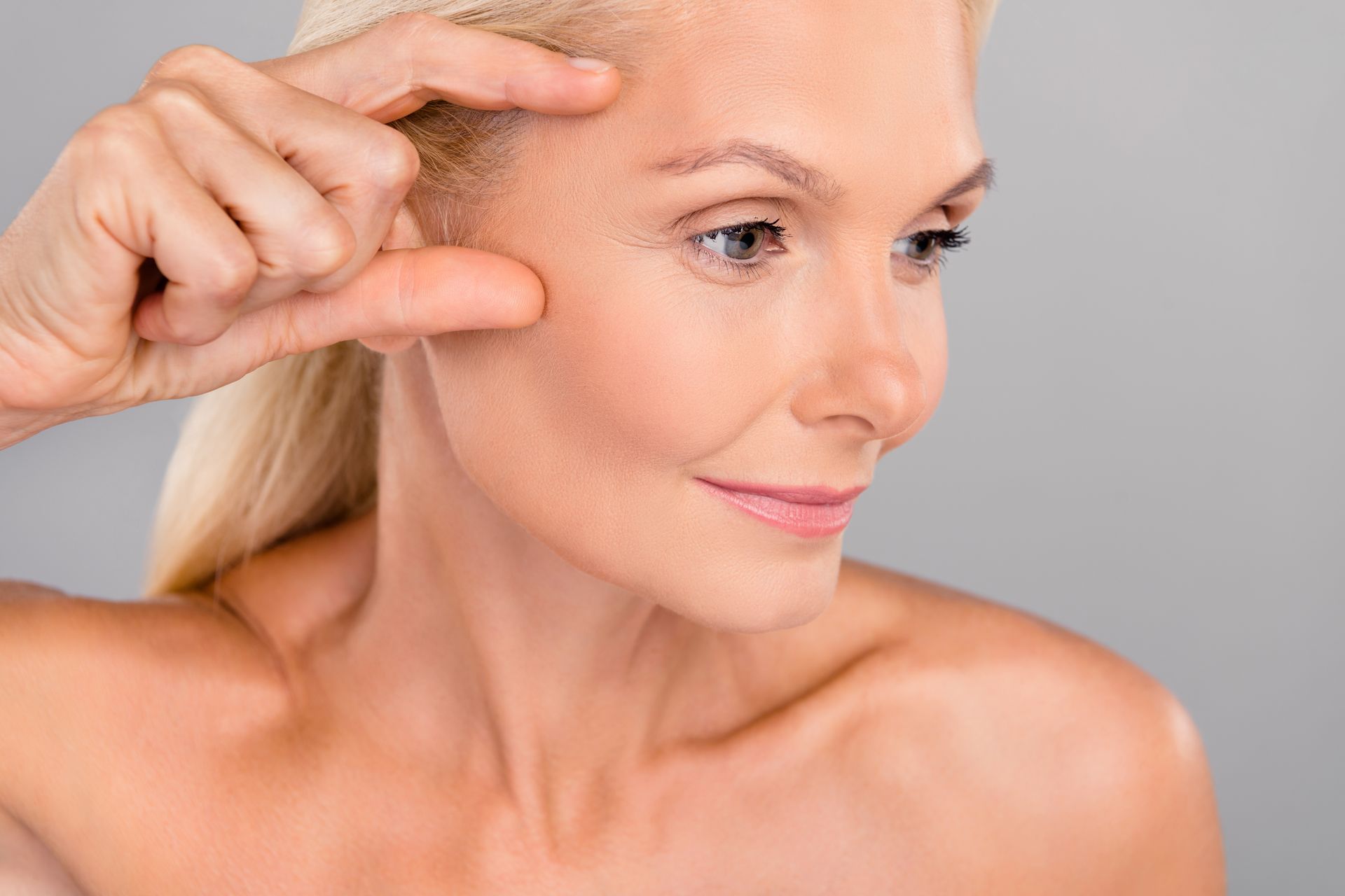 Woman touching skin near her eye, examining a facial wrinkle in soft studio lighting