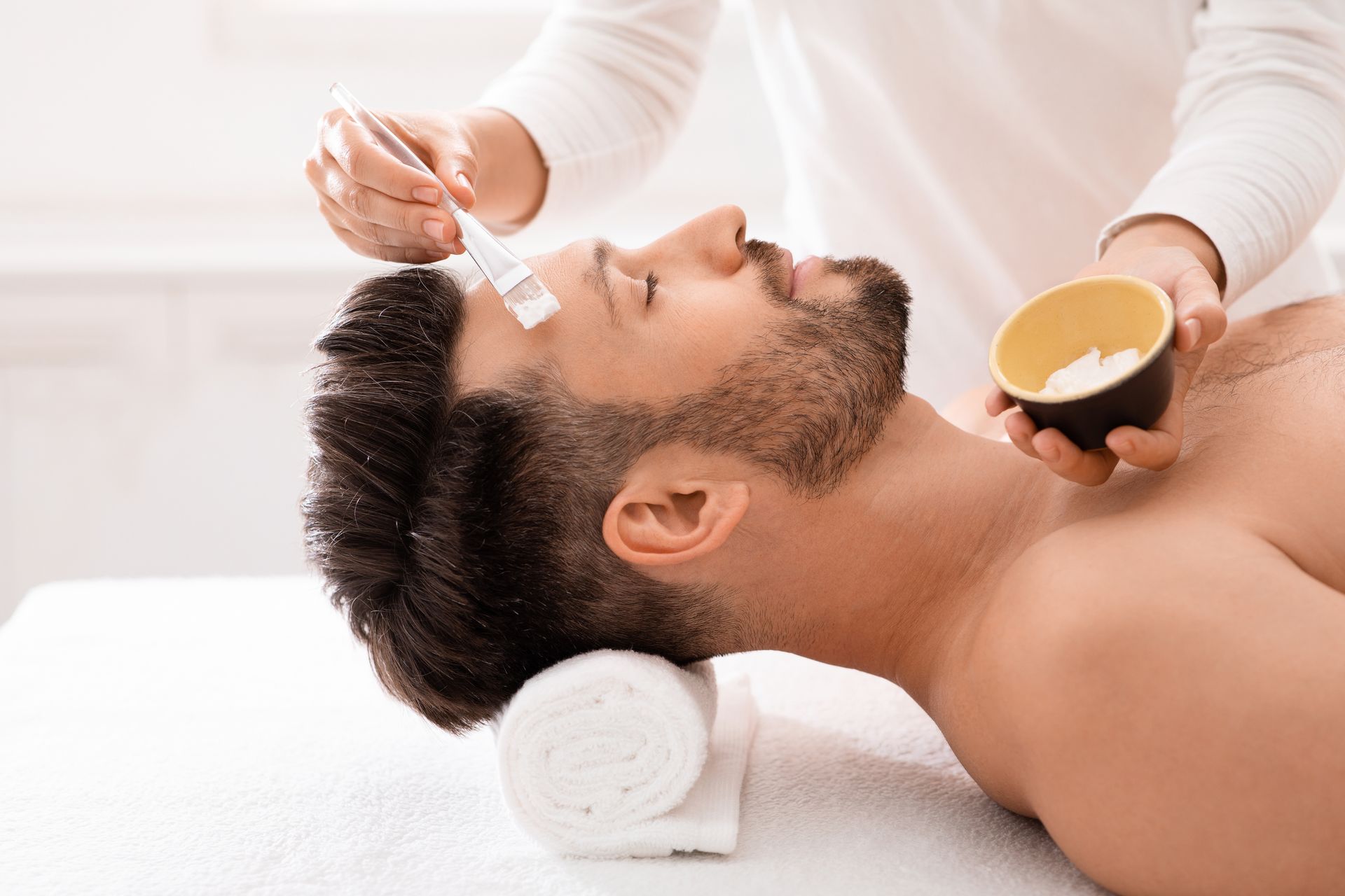 Spa facial treatment with a man receiving a brush mask while lying on a massage table