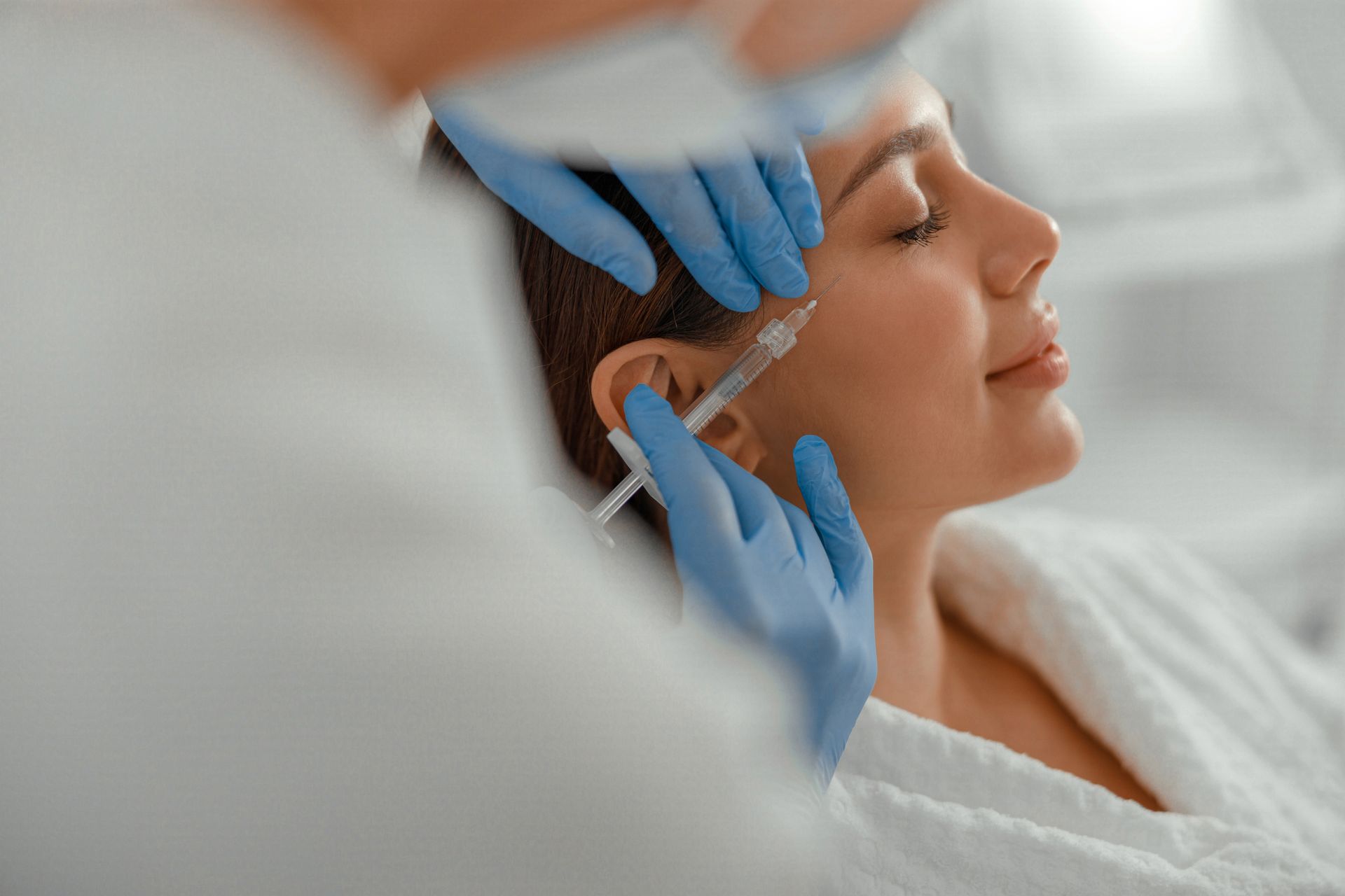 A woman receiving a facial injection near her cheekbone; doctor wearing blue gloves.