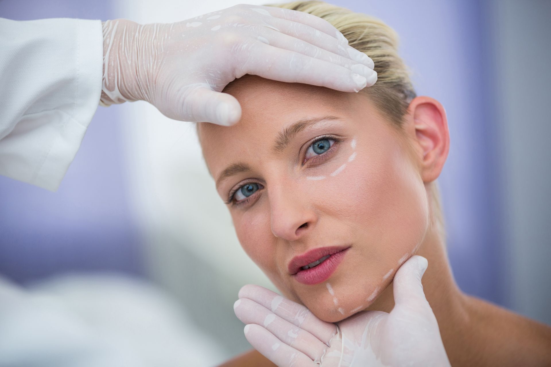 Woman with markings on face, in a medical setting, being examined by gloved hands.