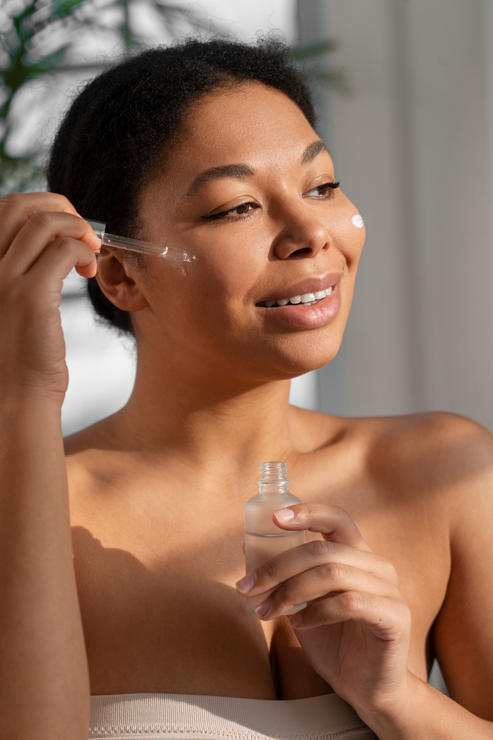 Woman applying skincare serum with a dropper. She smiles. Sunlight.