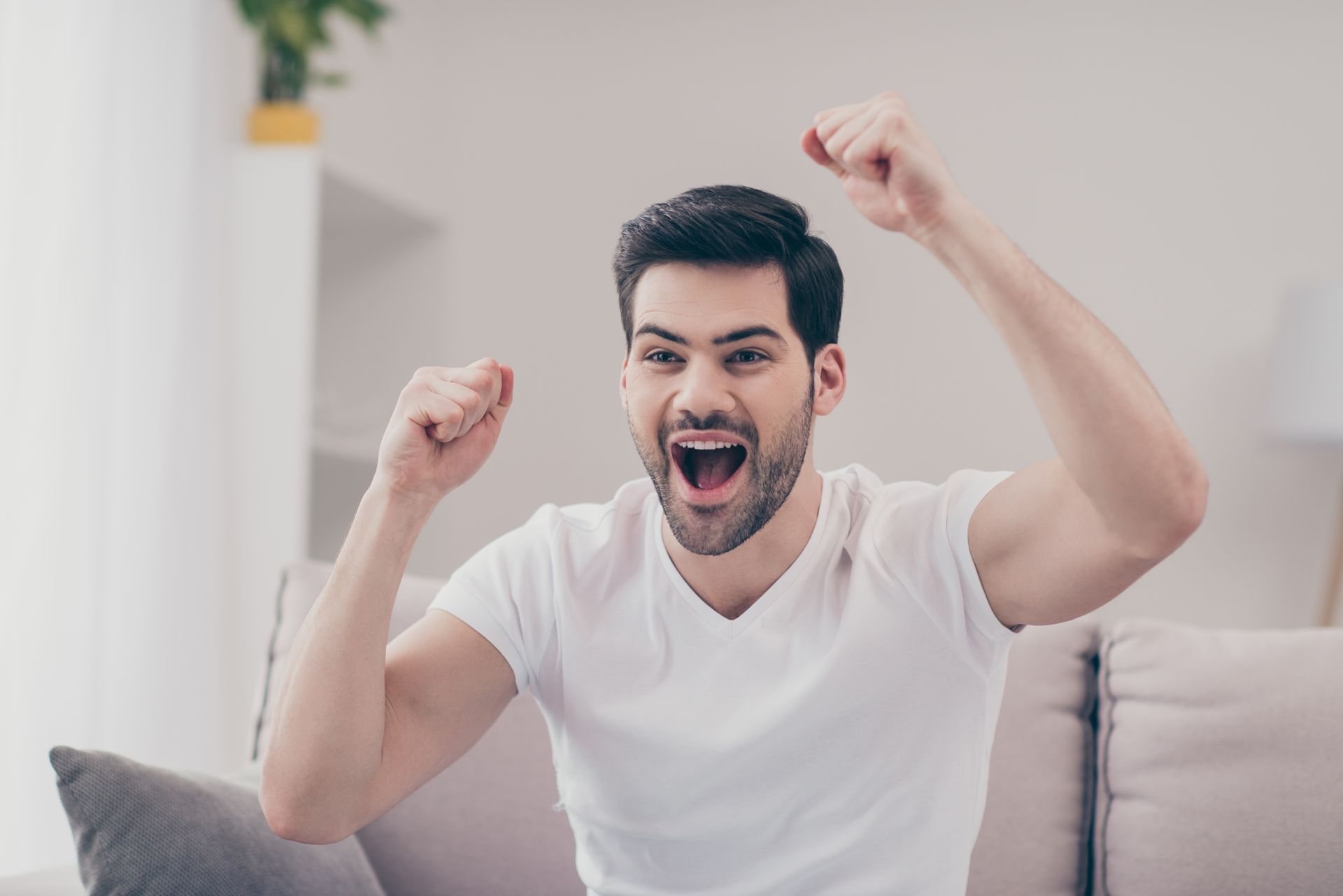 Cheering person on couch with raised fists in a bright living room