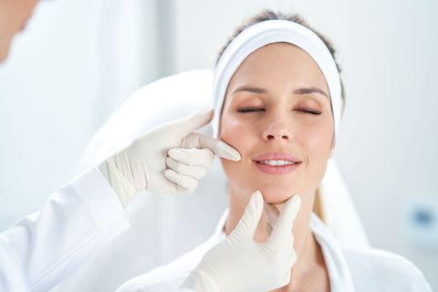 Woman receiving facial examination, hands of a doctor in gloves on her face in a medical setting.