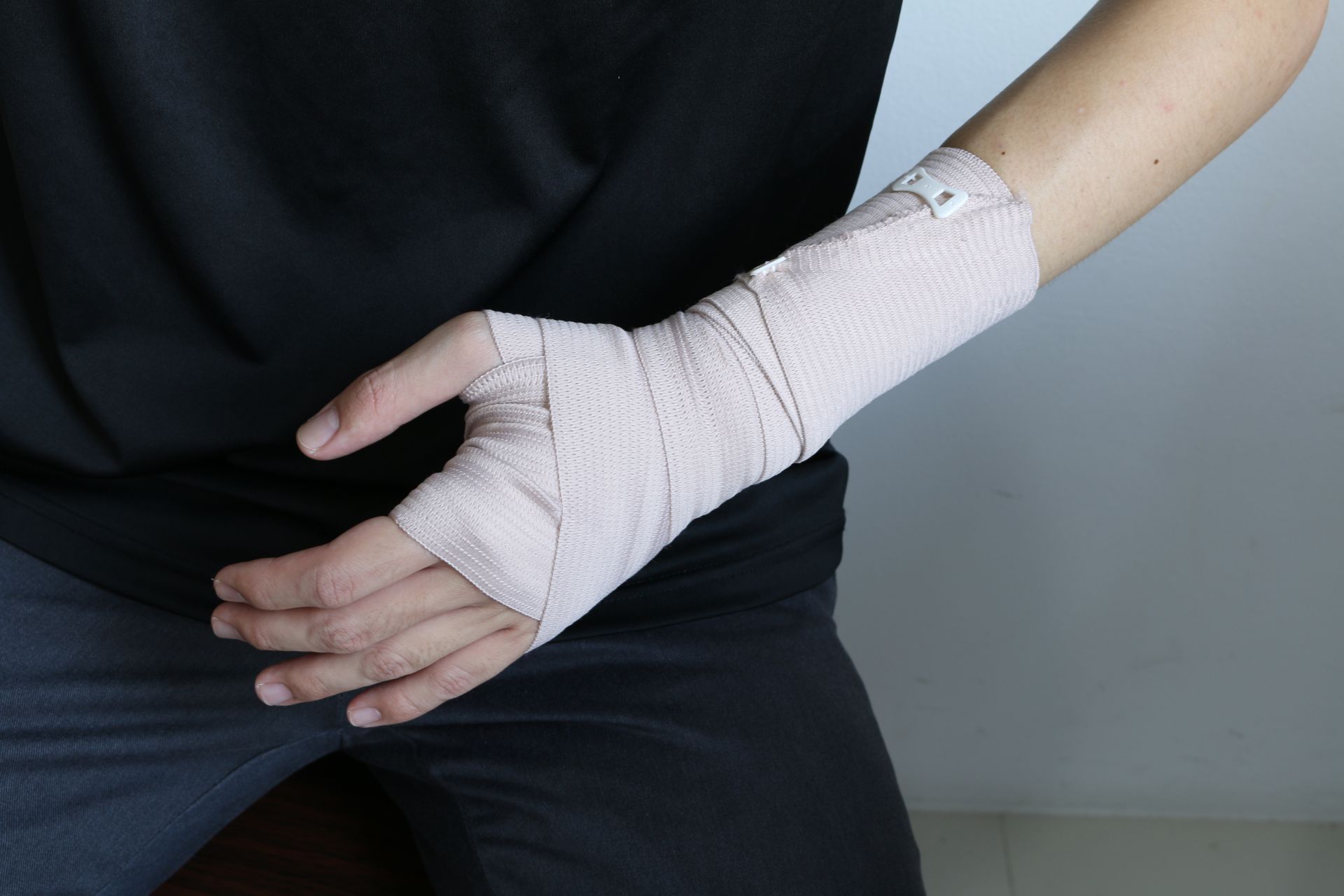Person's left wrist wrapped in beige bandage, hand extended, wearing black shirt and pants.