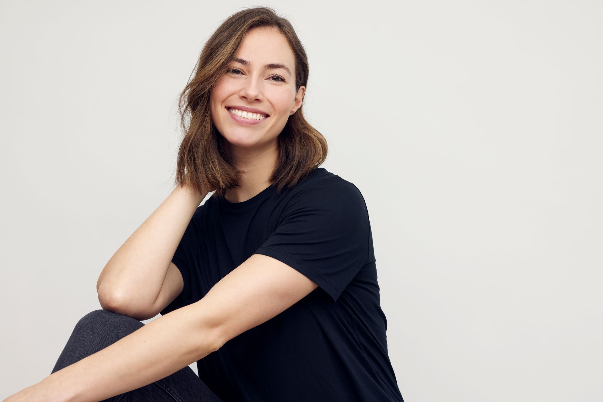 Woman with short brown hair smiling, wearing a black t-shirt, posing against a white background.