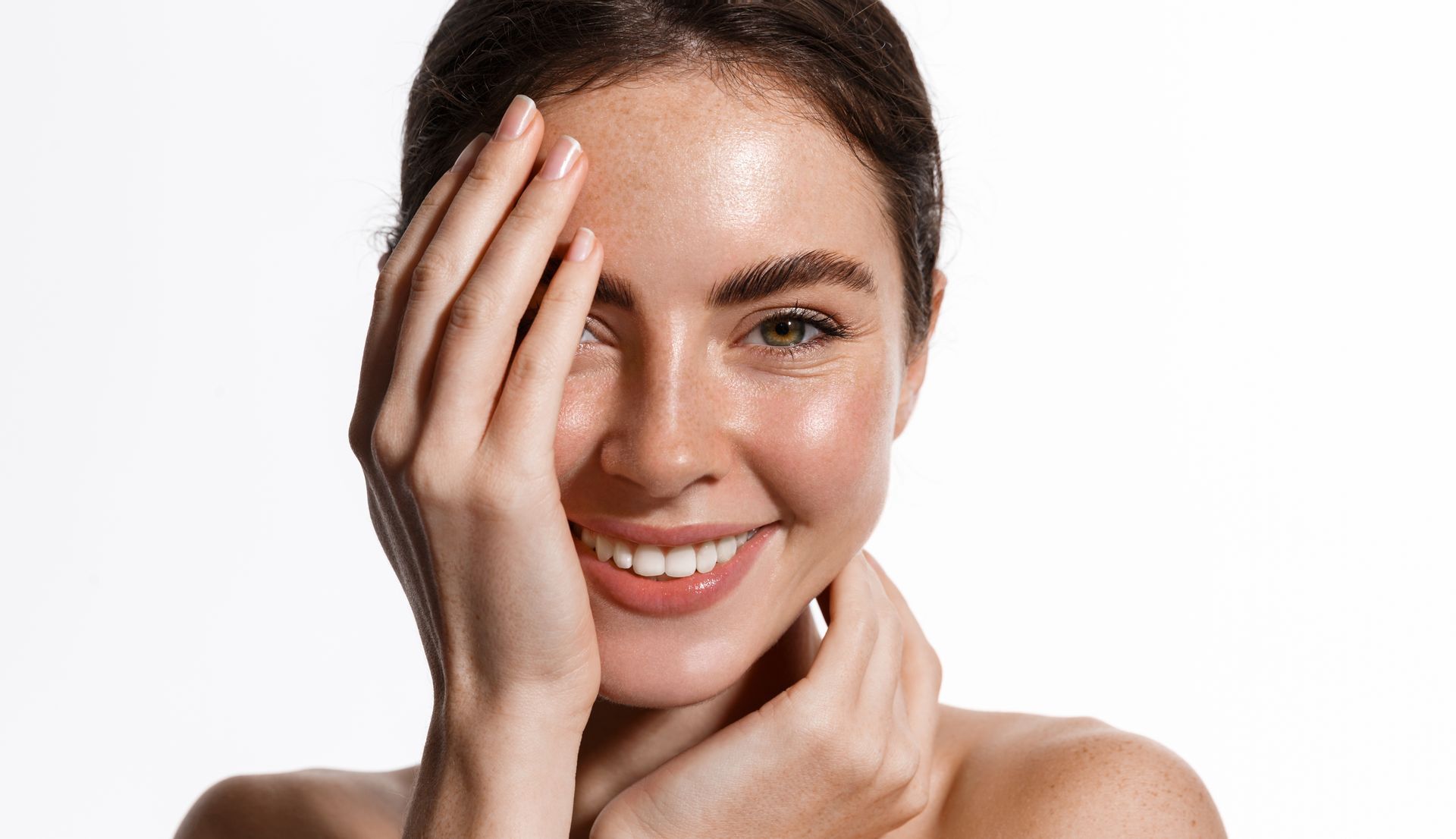 Woman with a joyful expression, hand on face, glowing skin, white background.