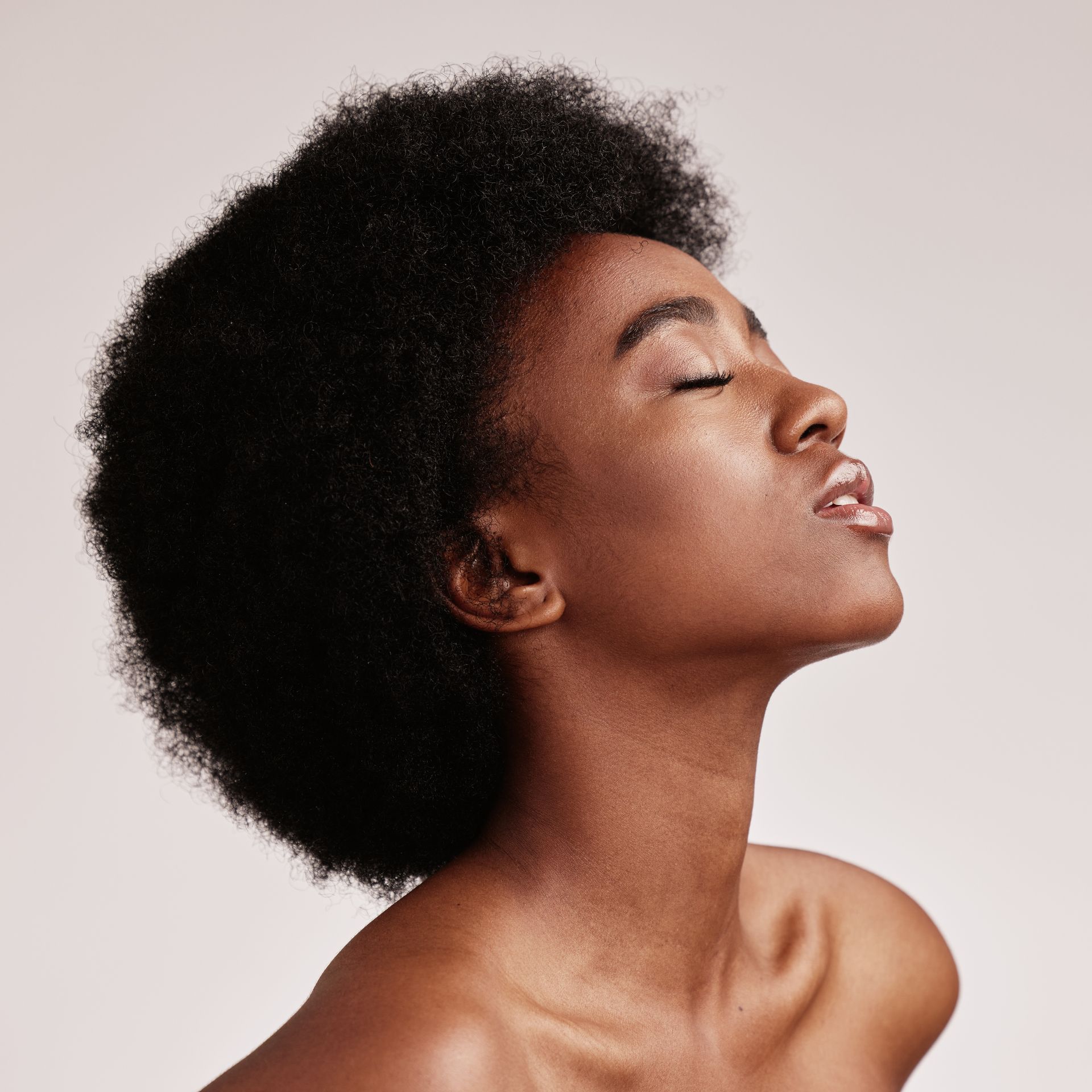 Black woman with closed eyes, head tilted back, radiant skin, against a light background.