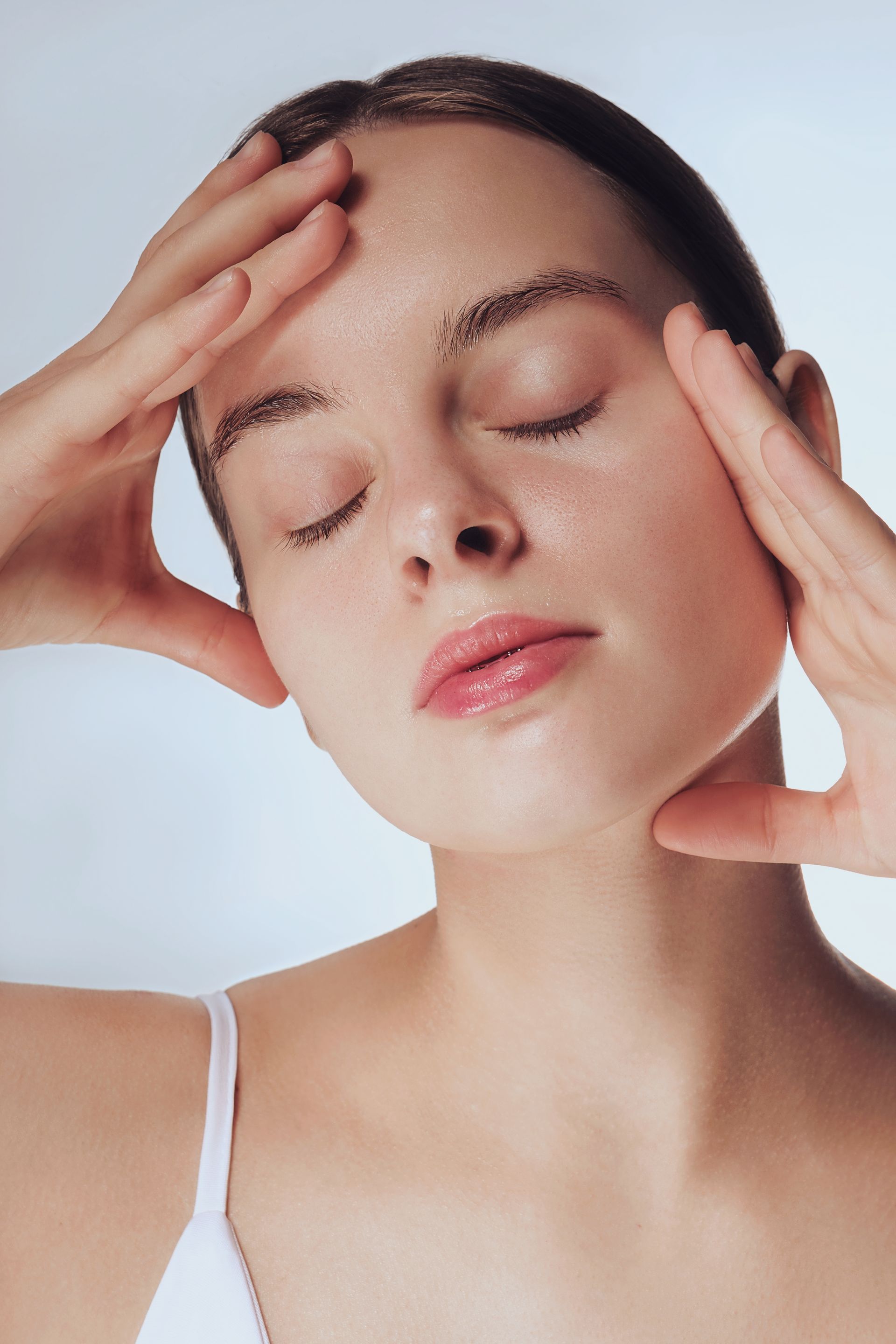 Woman with eyes closed, hands on face, bathed in soft light.