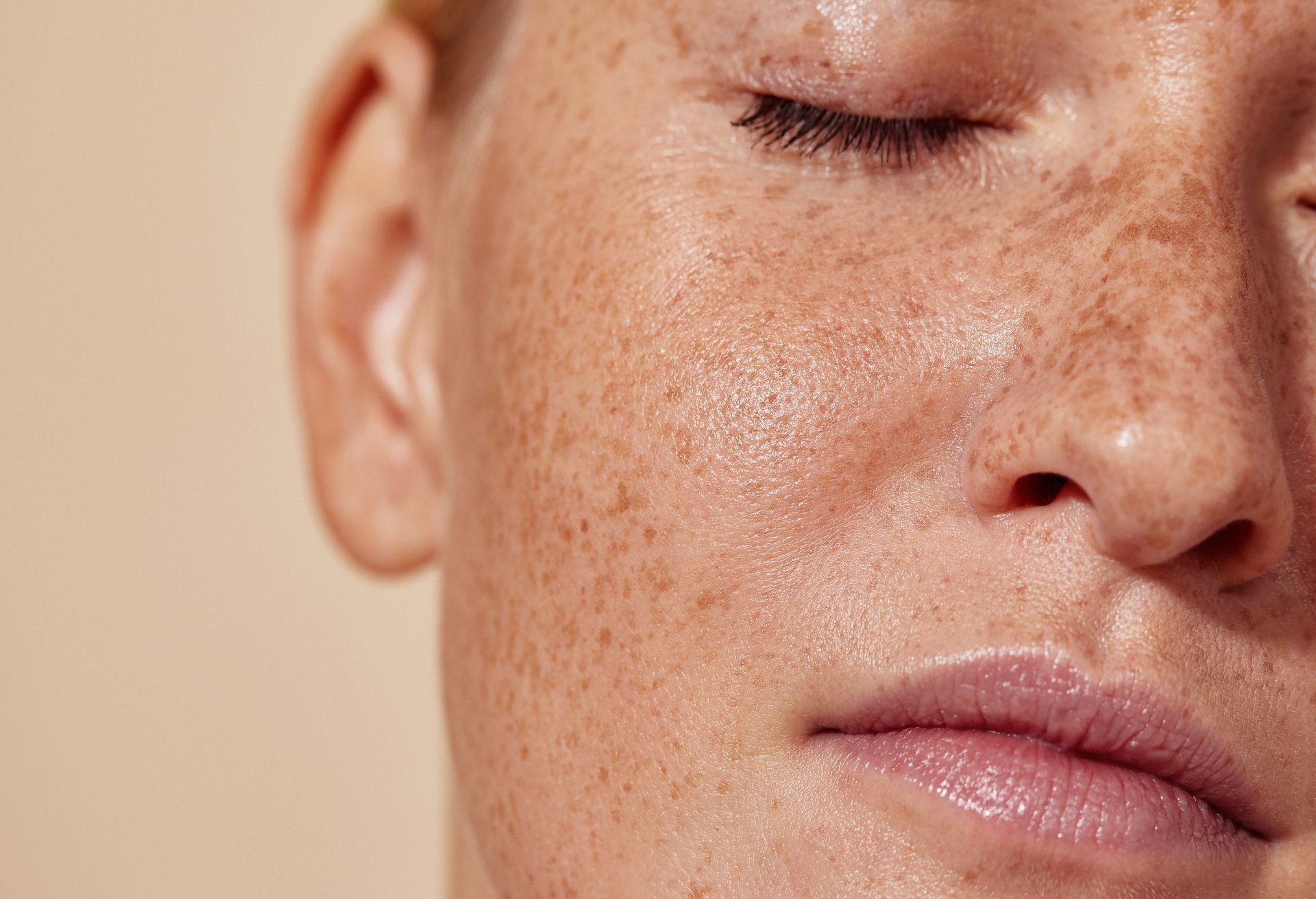 Close-up of a person's face with freckles, closed eyes, and dewy skin.