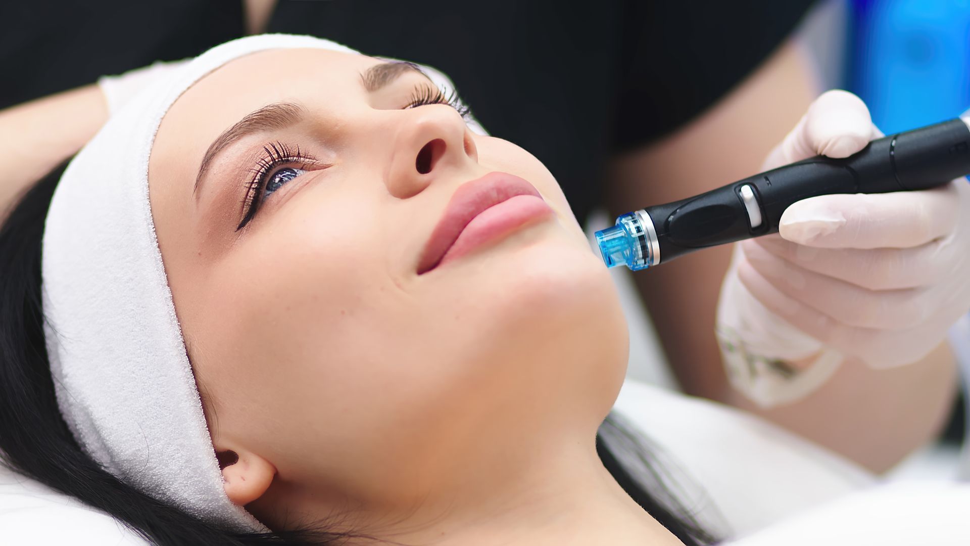 Woman receiving a facial treatment with a handheld device, in a medical setting.