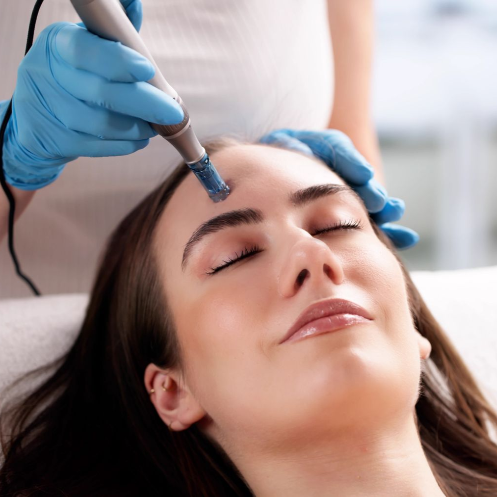 Woman receiving facial treatment with closed eyes; a gloved hand uses a device on her forehead.