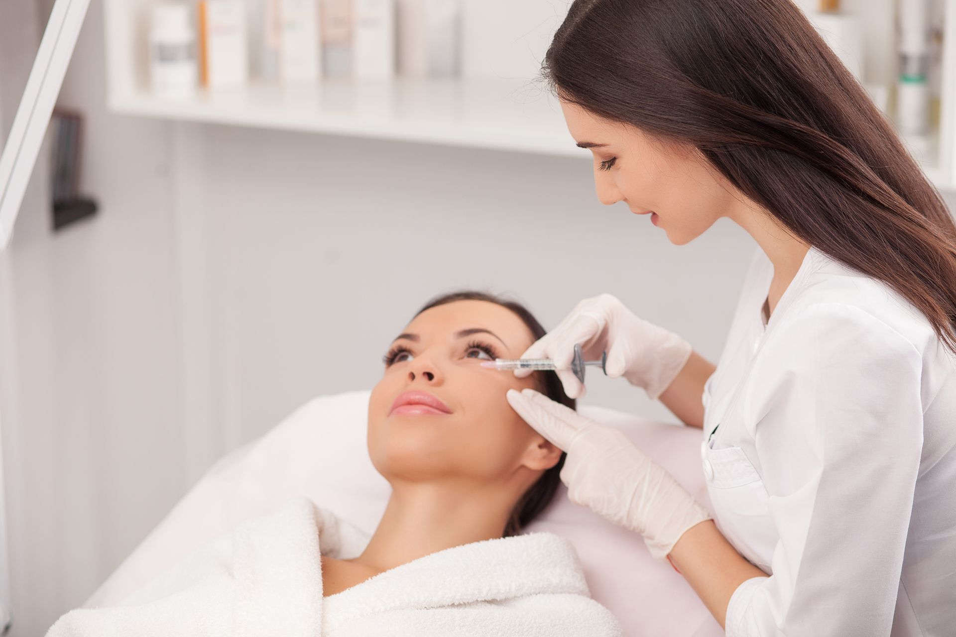 Woman receiving cosmetic injection near her eye in a medical office.