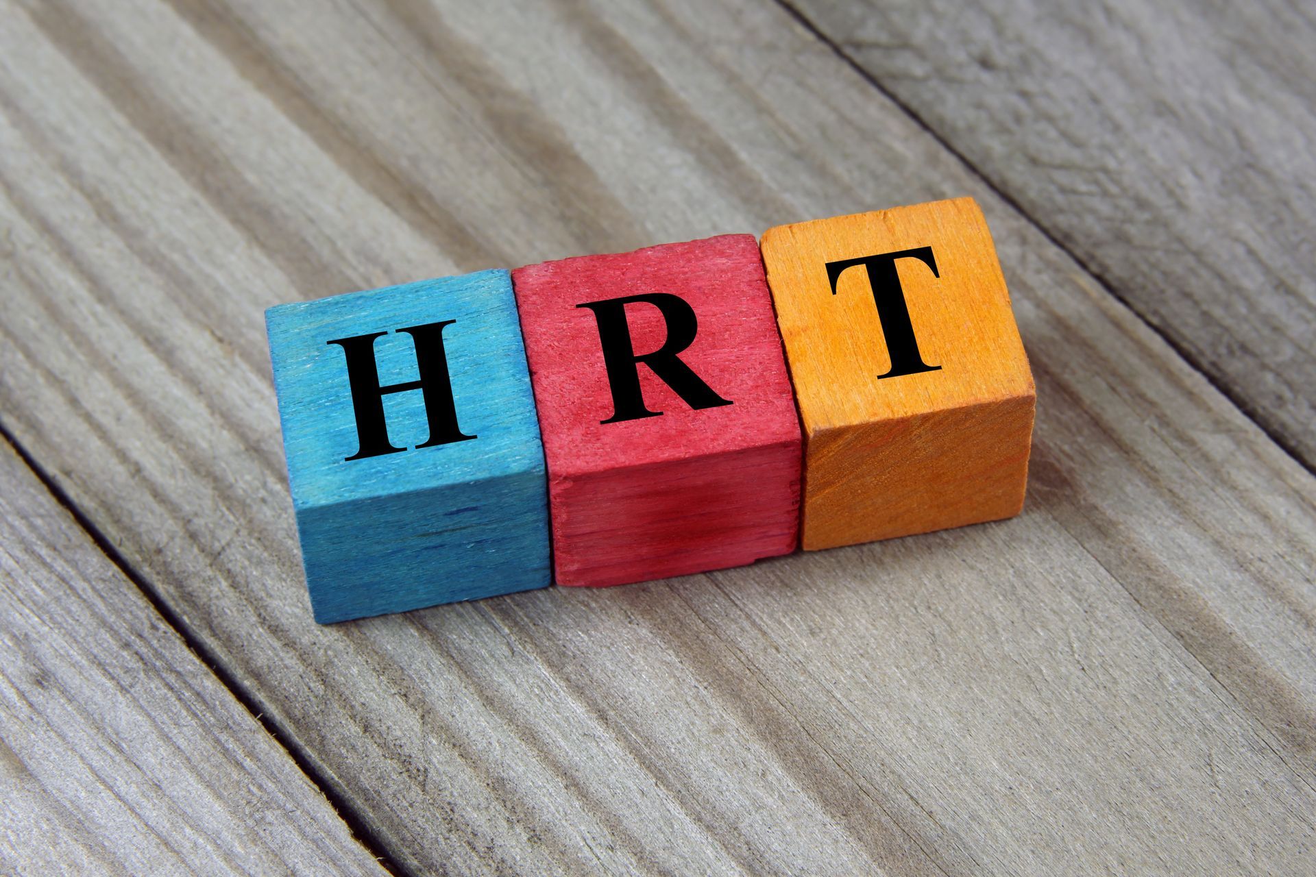 Three colored wooden blocks on a wooden surface spelling HRT