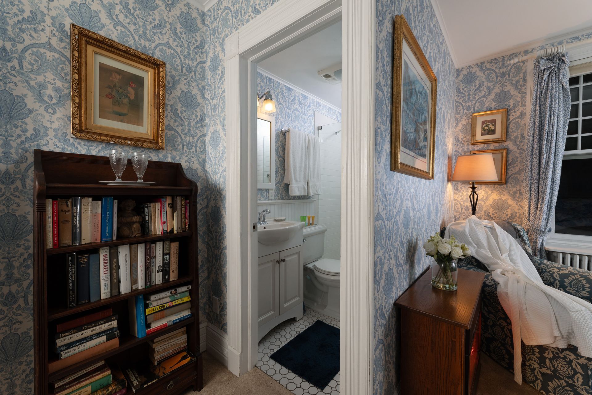 A living room with a bookshelf and a chair and a bathroom.