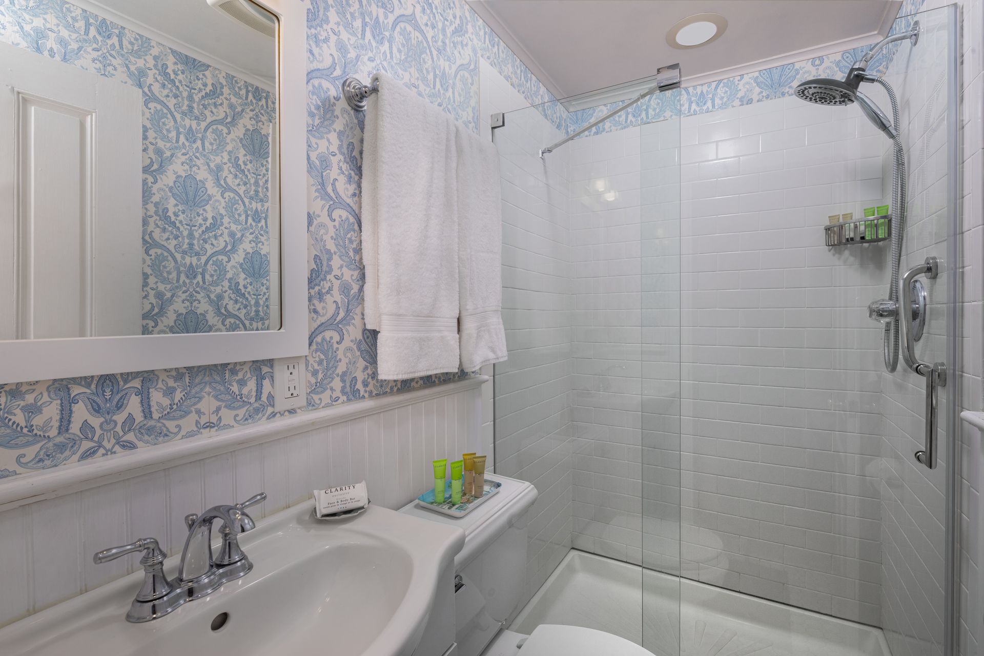 A bathroom with a sink , toilet , shower and mirror.