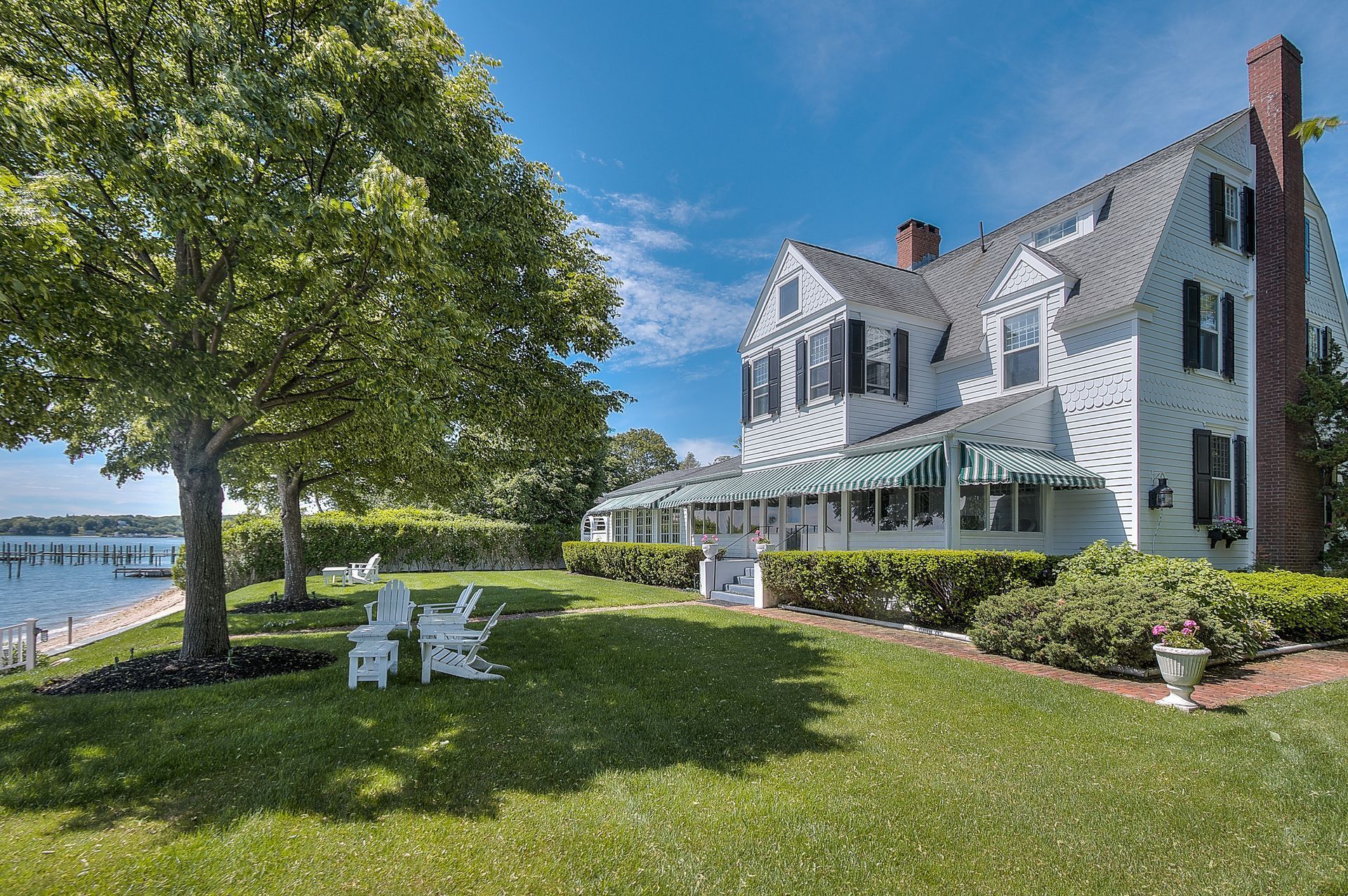 White house with black shutters, green lawn, waterfront view, blue sky.