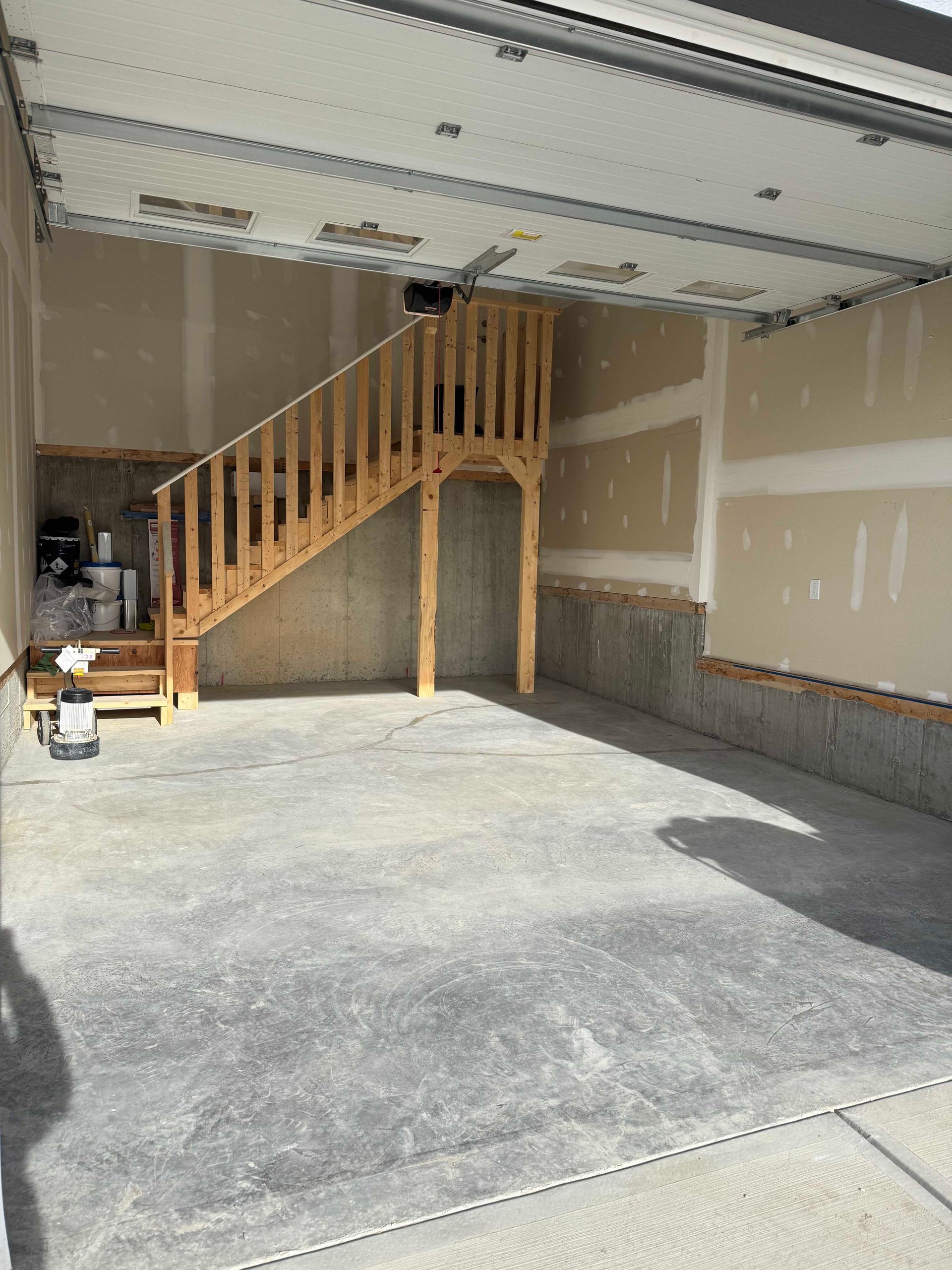 Empty garage with concrete floor, unfinished walls, and a wooden staircase leading to a loft.