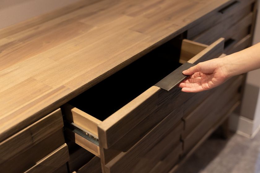Hand opening a wooden dresser drawer under a wood countertop