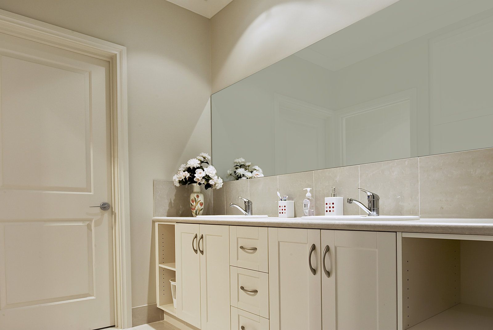 Bathroom vanity with mirror, white cabinets, sink, and flowers on the counter