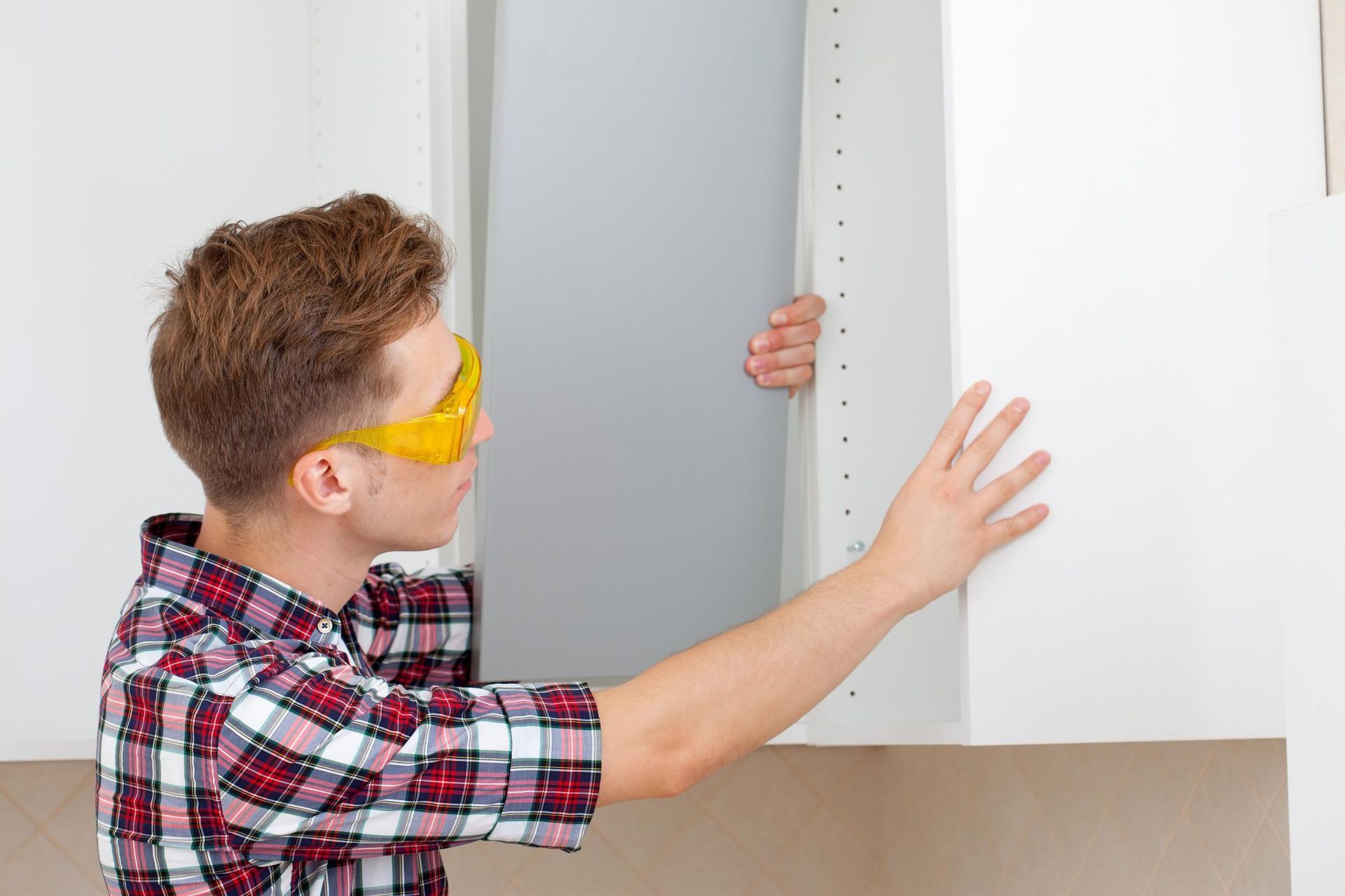 Person measuring a white cabinet with a ruler while wearing yellow safety glasses
