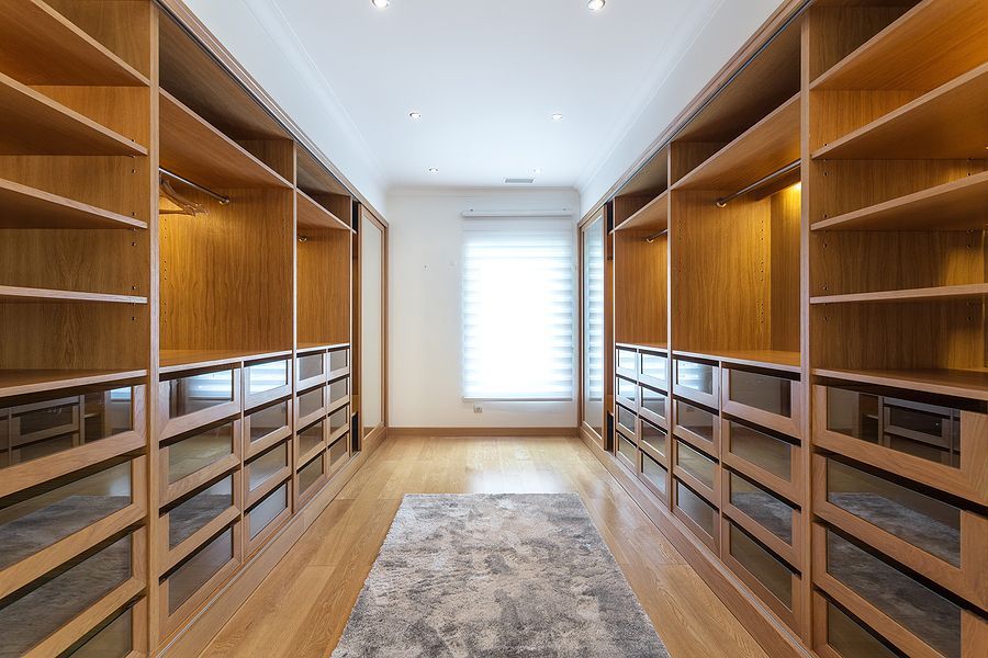 Walk-in closet with wooden shelves and drawers lining both sides, carpet runner, and a window at the end.