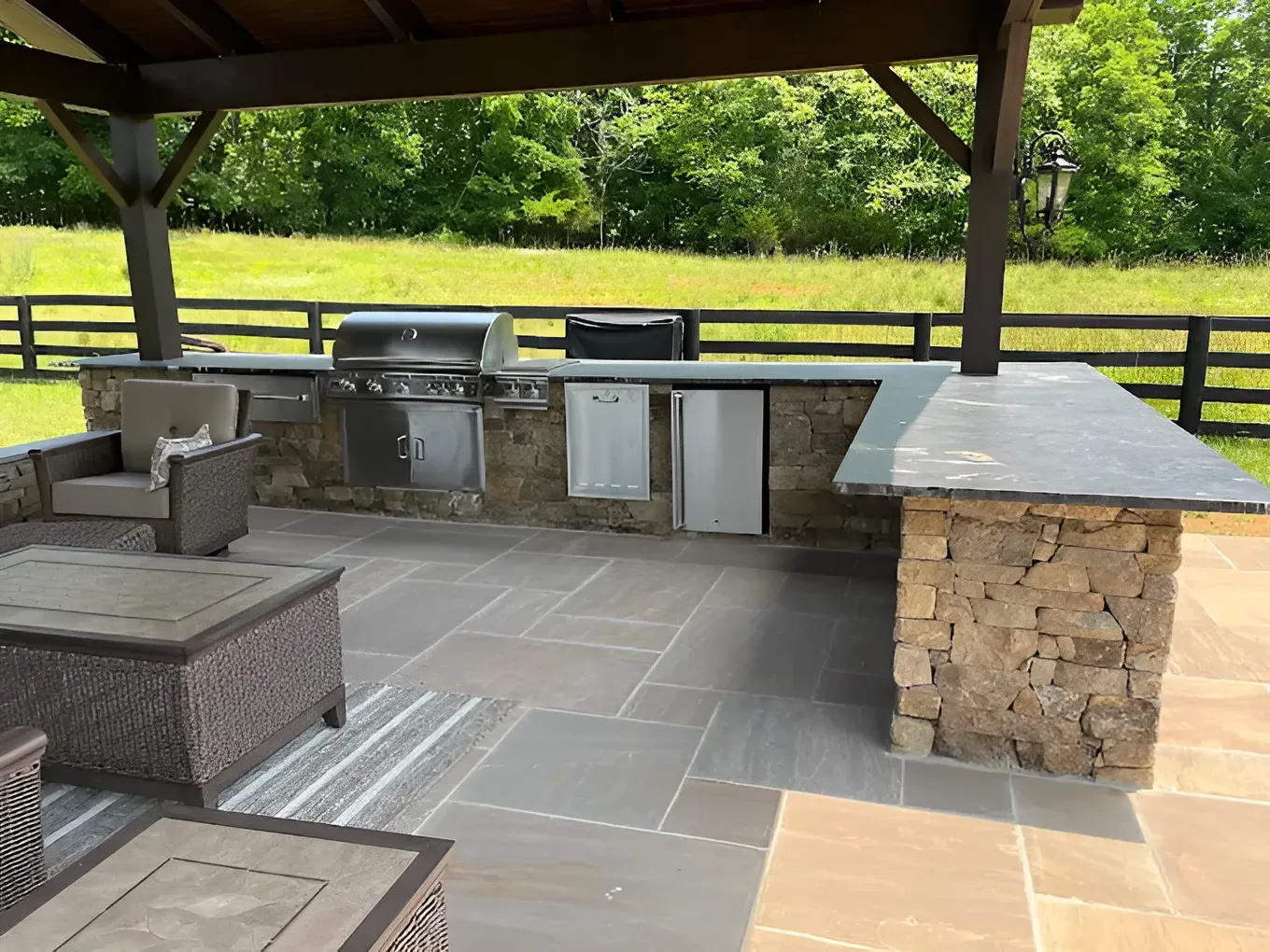 Covered outdoor kitchen with stone counters, grill, and patio seating on a paved terrace.