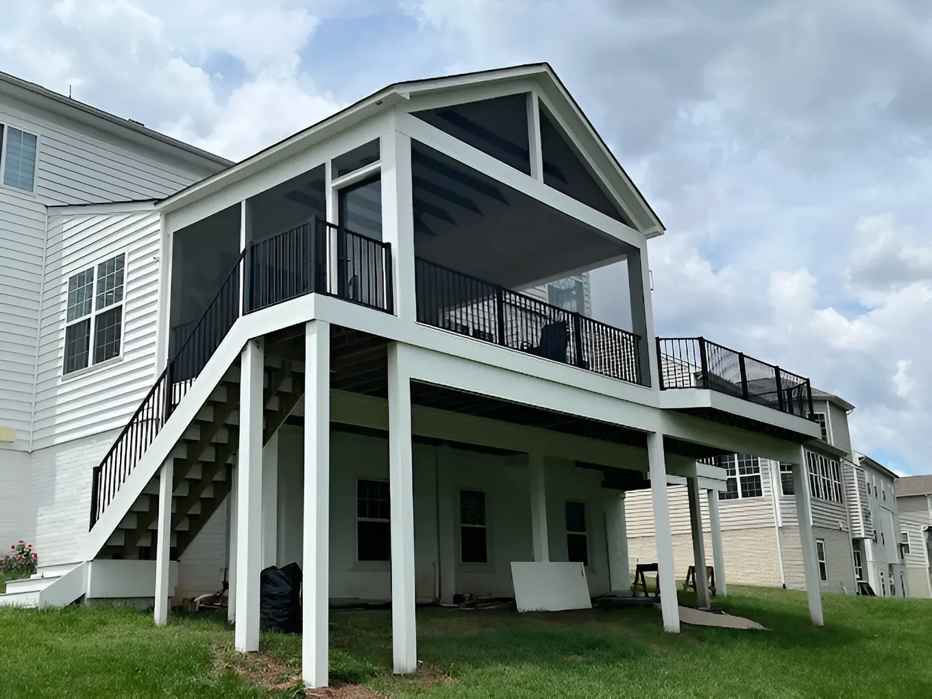 Raised coastal house with white siding, green trim, and covered porches on stilts under a cloudy sky
