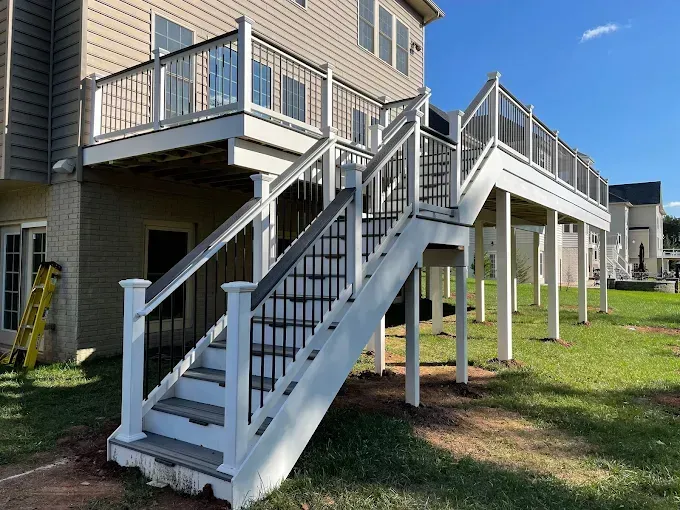 Outdoor apartment stairways and raised decks on beige buildings, with white railings and grassy ground below