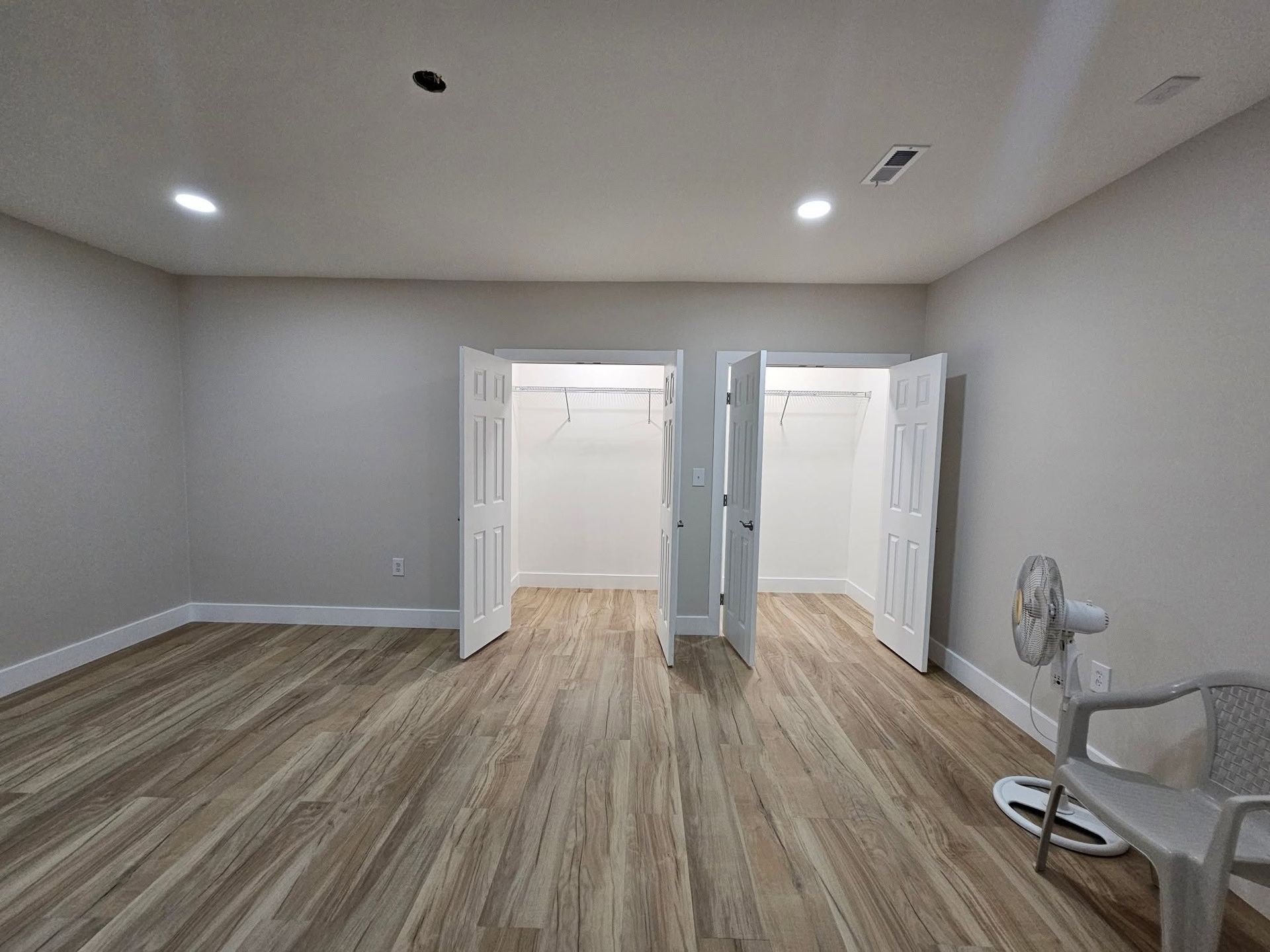 Empty room with light wood flooring, gray walls, and open double doors to a bright adjoining space