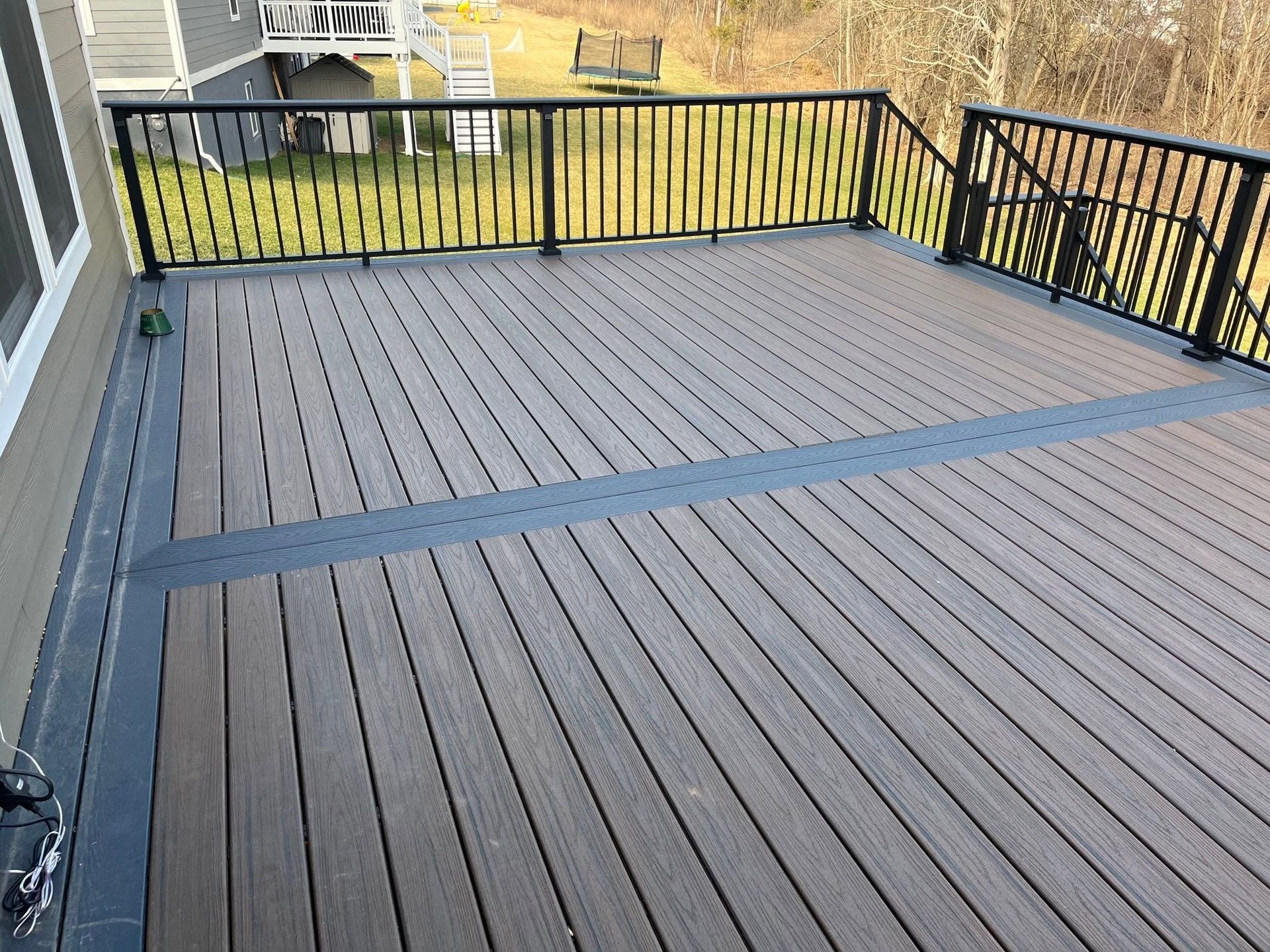 Spacious gray deck with black metal railing and a yellow yard beyond.
