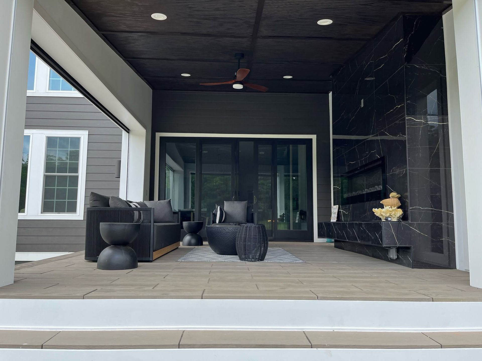 Covered patio with dark outdoor furniture, fireplace, and sliding glass doors leading to a home interior