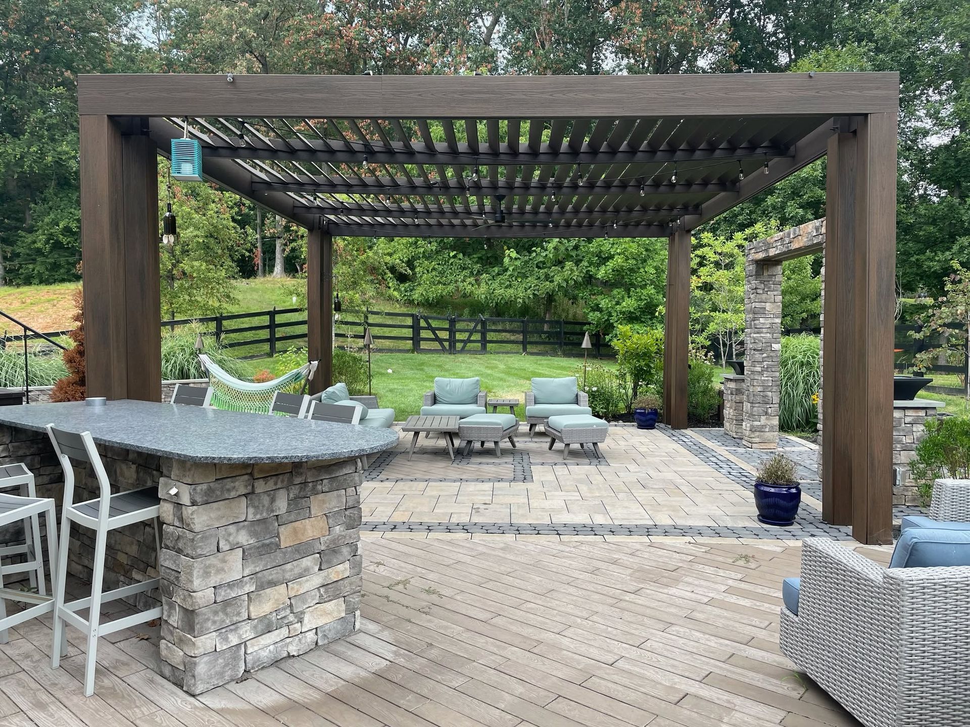 Outdoor patio with pergola, stone bar, lounge chairs, and backyard greenery