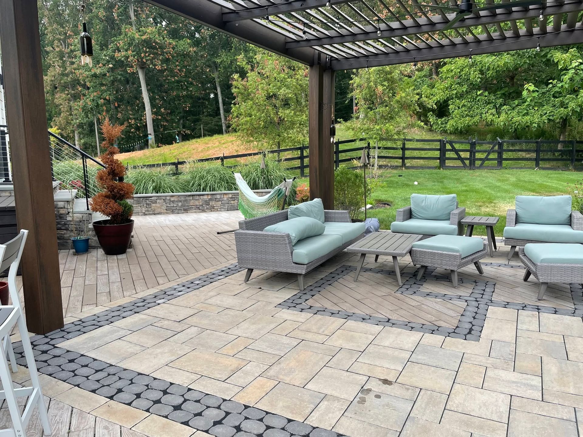 Covered patio with light blue outdoor seating on a stone tile floor, overlooking a green yard and wooden fence