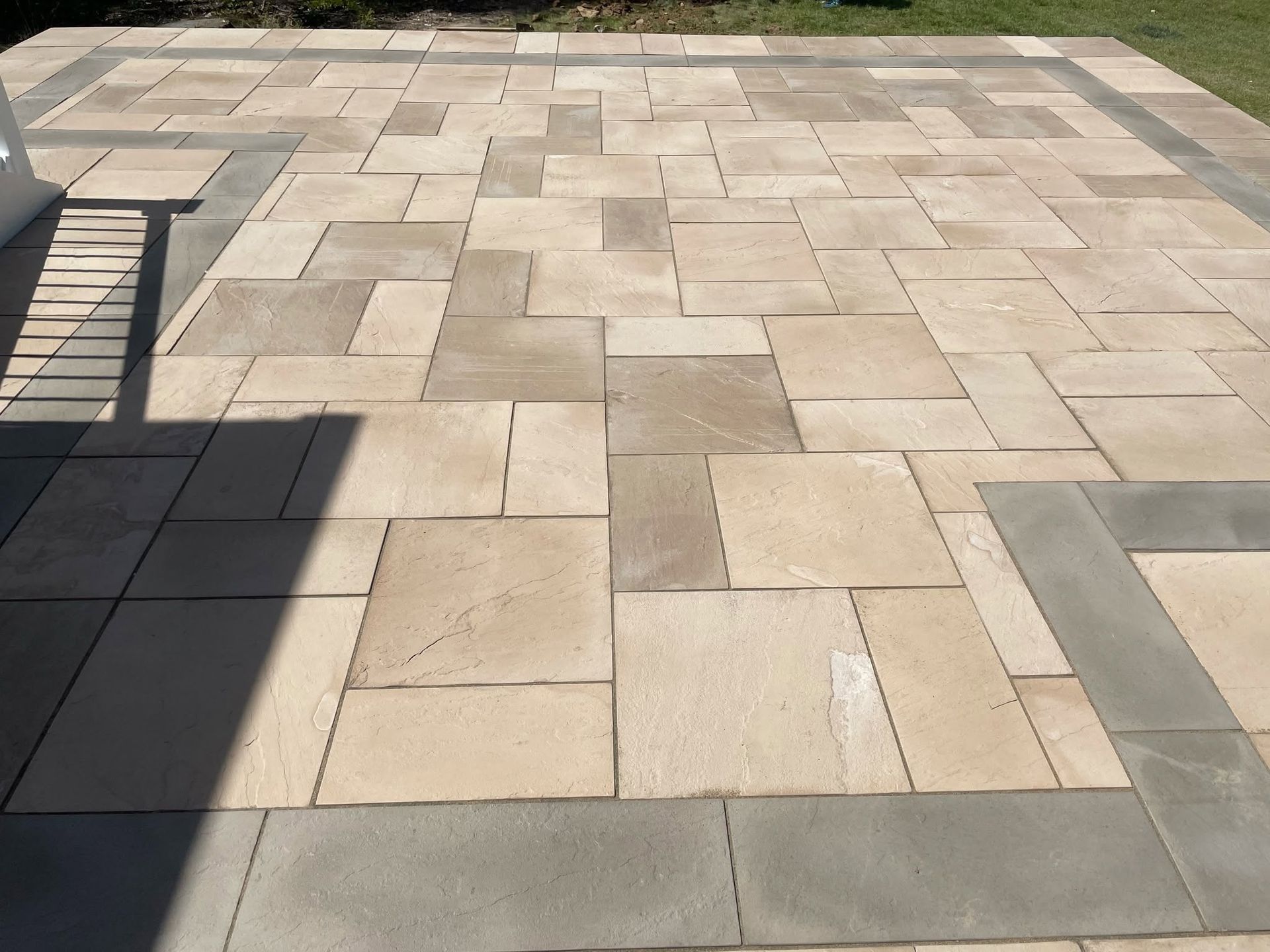 Stone-tiled patio with beige and gray pavers in sunlight, bordered by a bench on the left.