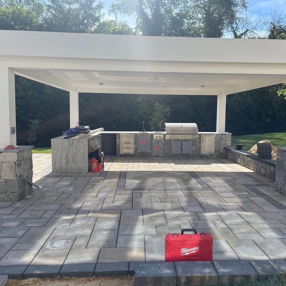 Outdoor stone patio with built-in grill and cabinets under a white pavilion, red tool bag in foreground