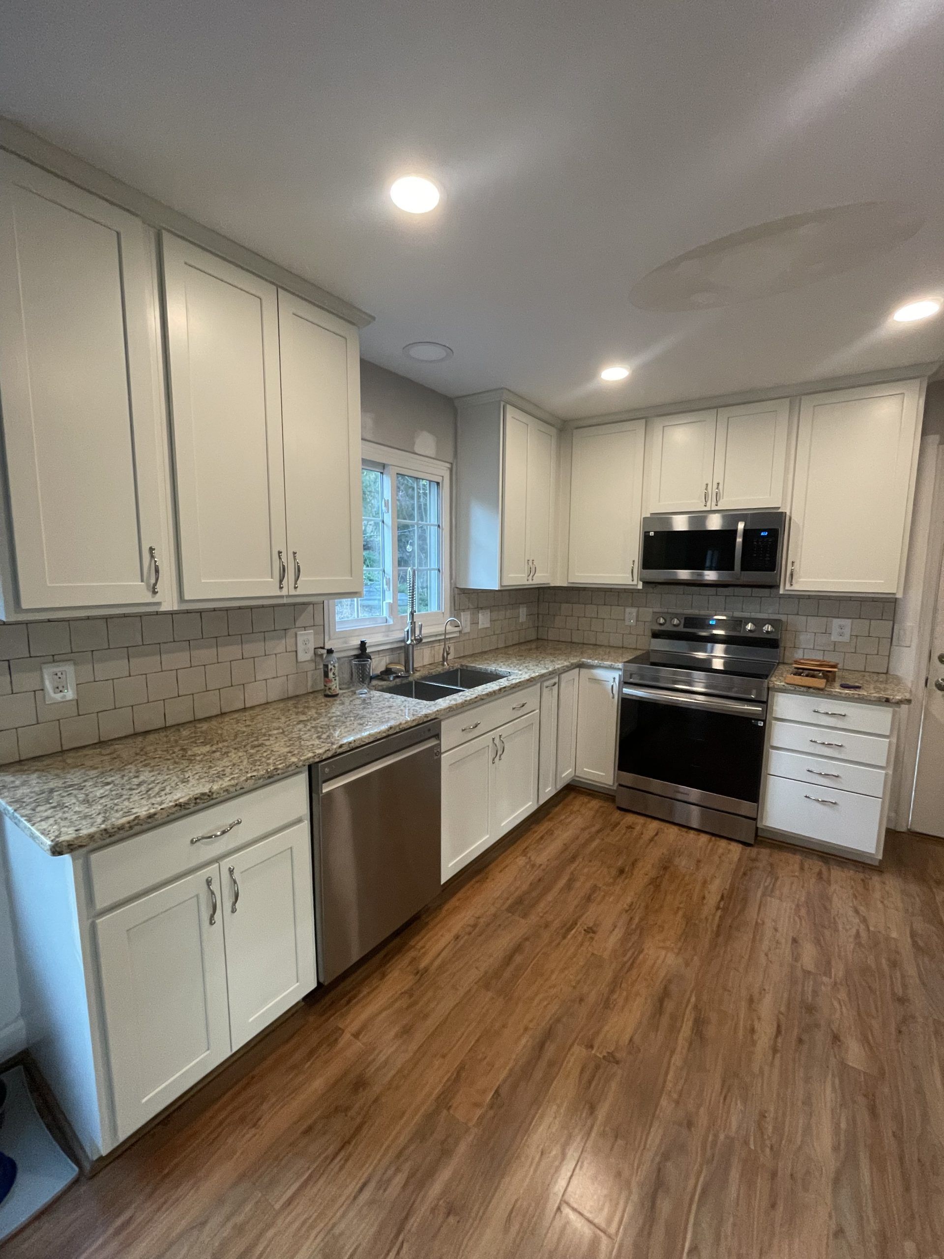 Bright kitchen with white cabinets, granite counters, stainless appliances, and wood-look flooring.