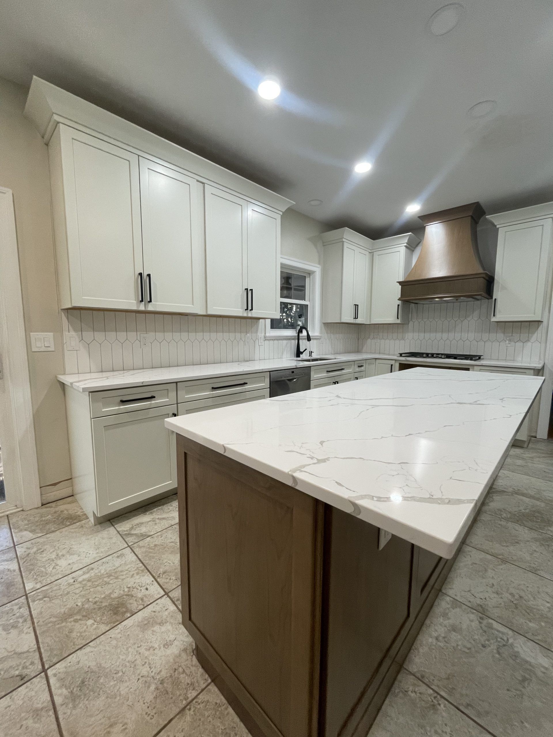 Bright modern kitchen with white cabinets, marble island, and stainless range hood