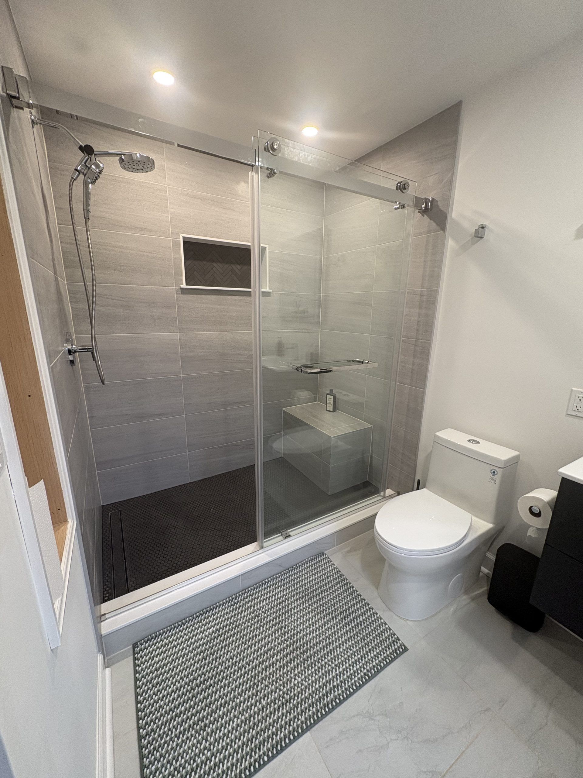 Small bathroom with a glass shower, toilet, sink, and gray rug.