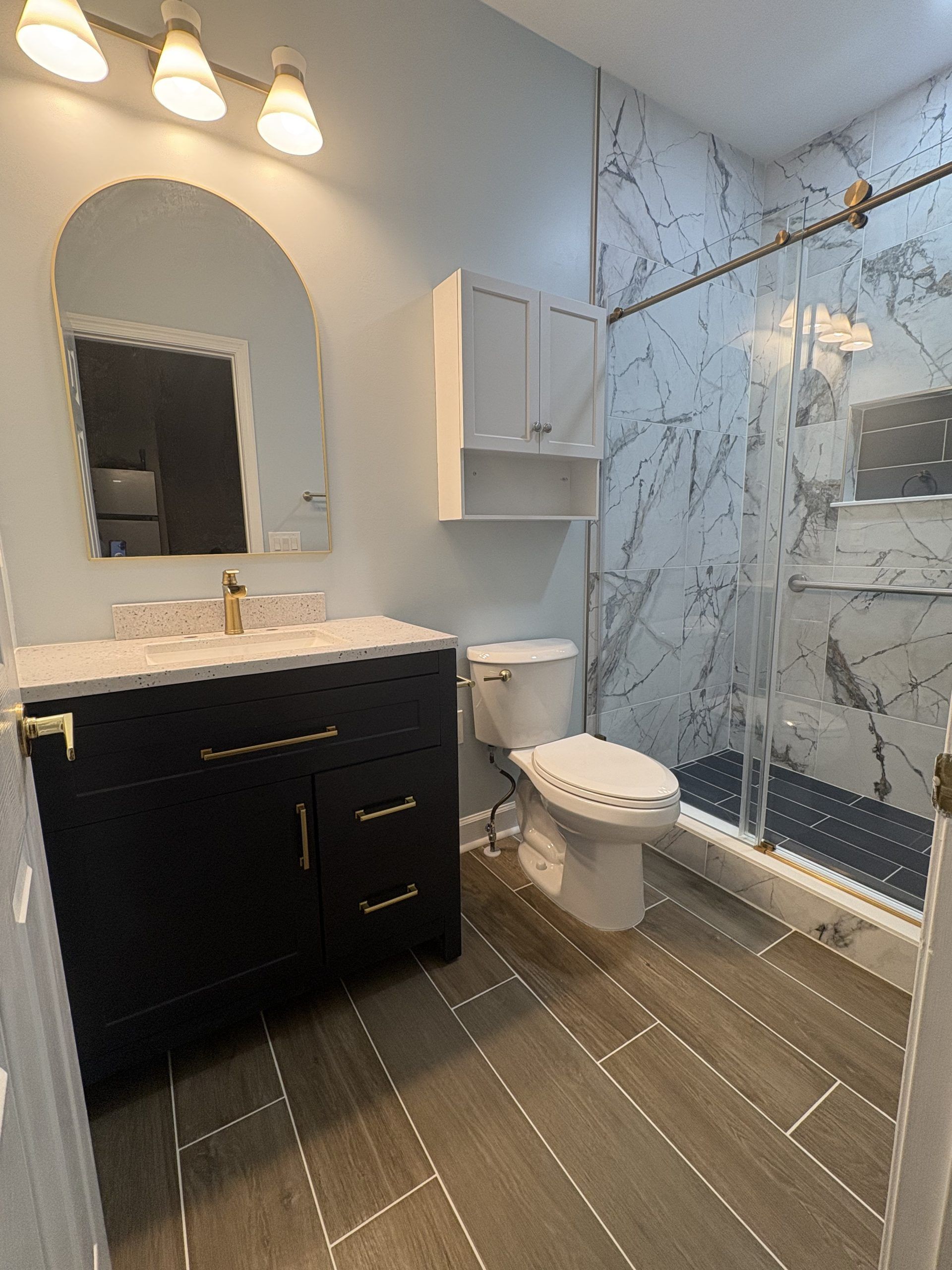 Modern bathroom with black vanity, marble shower, toilet, and beige tile floor