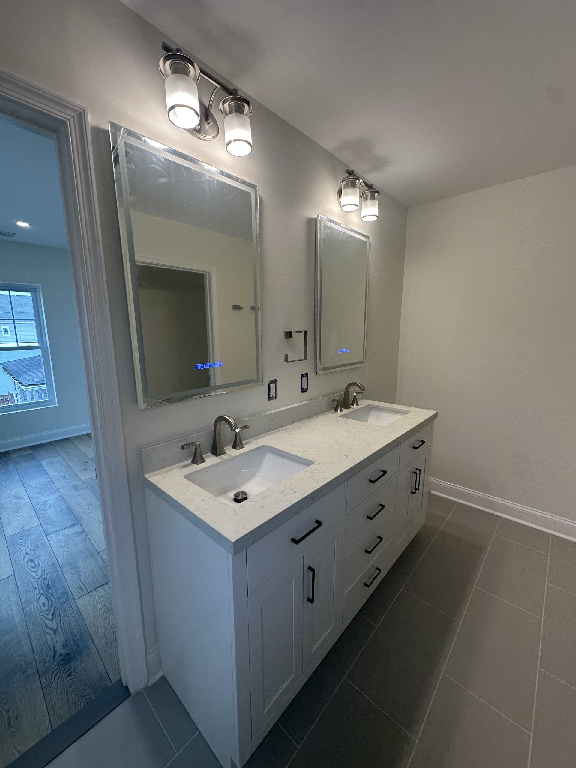 Bright modern bathroom vanity with double sinks, mirrors, and wall lights near a tiled shower area
