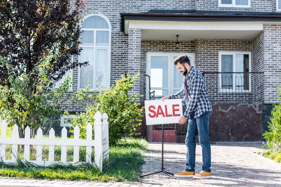 Man placing a SALE sign in front of a brick house. Man placing a SALE sign in front of a brick house.