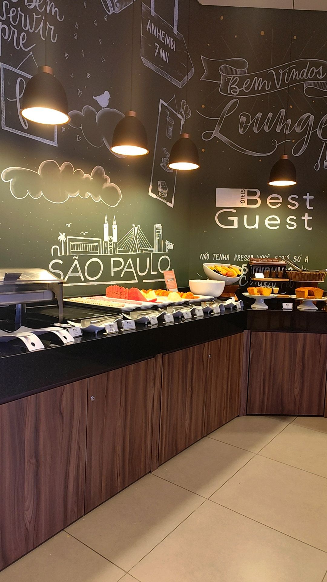 Área de buffet com comida exposta, parede escura com placas 